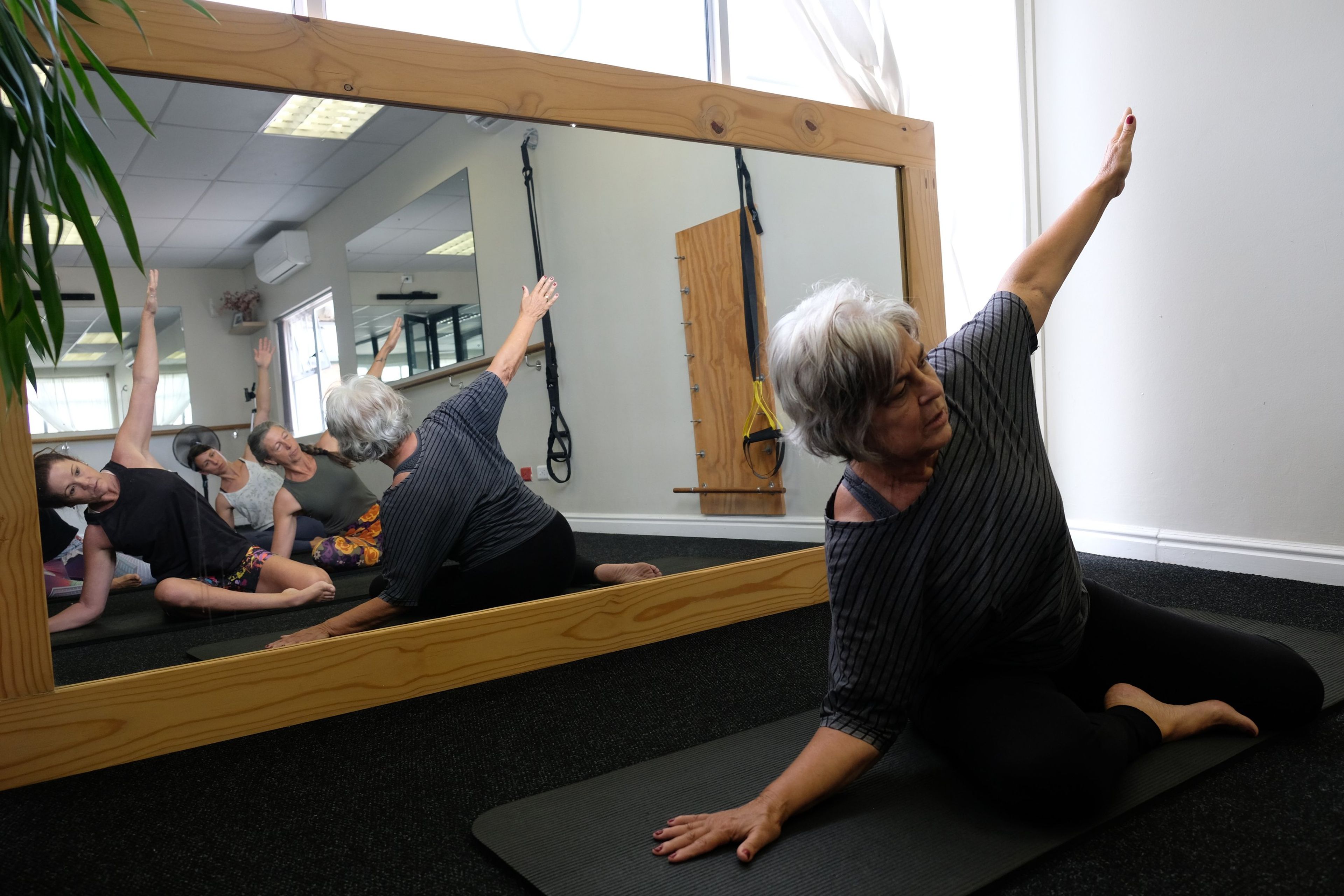 A participant in a seated side stretch, reflected in the studio's wooden-framed mirror