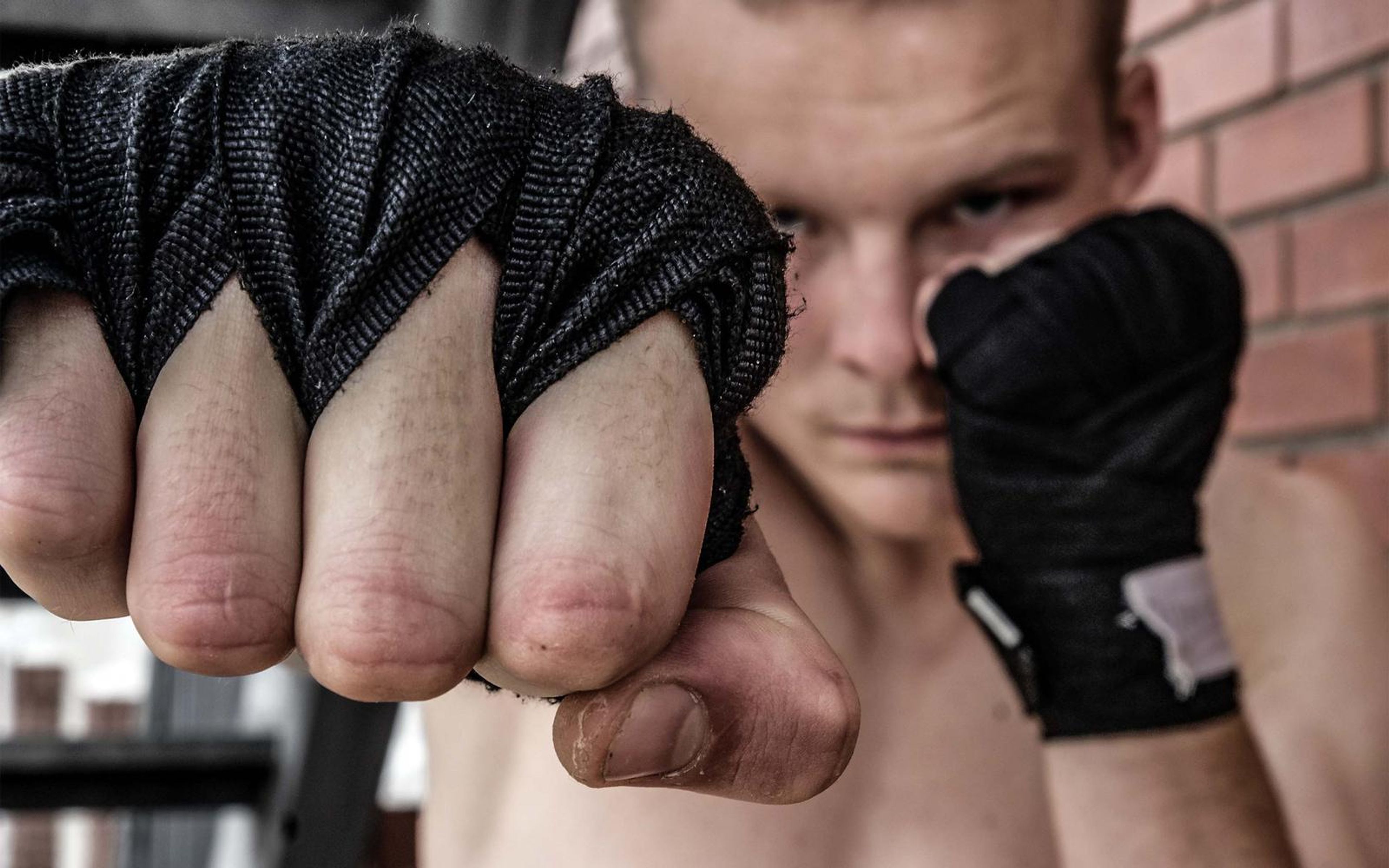 Fighter's wrapped fist thrust toward the camera with his face blurred behind it, red brick wall