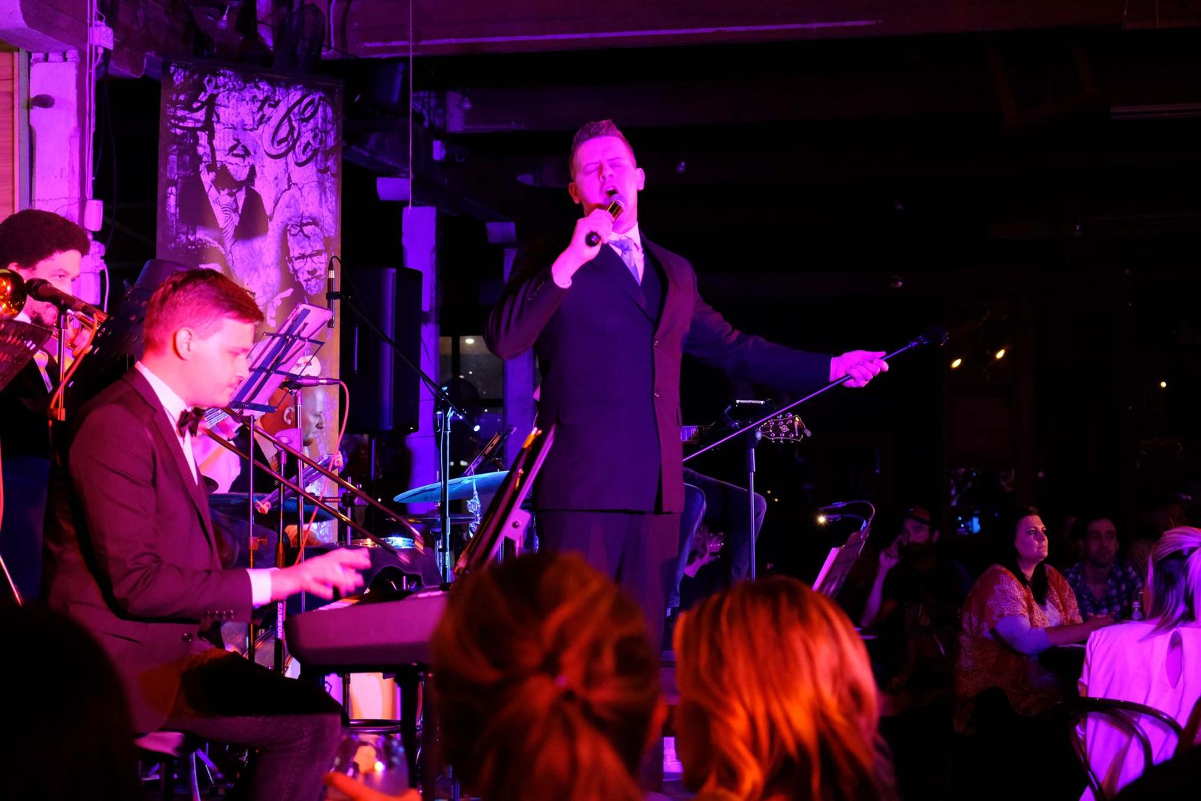 Singer in a suit performing with the keyboardist and horn players