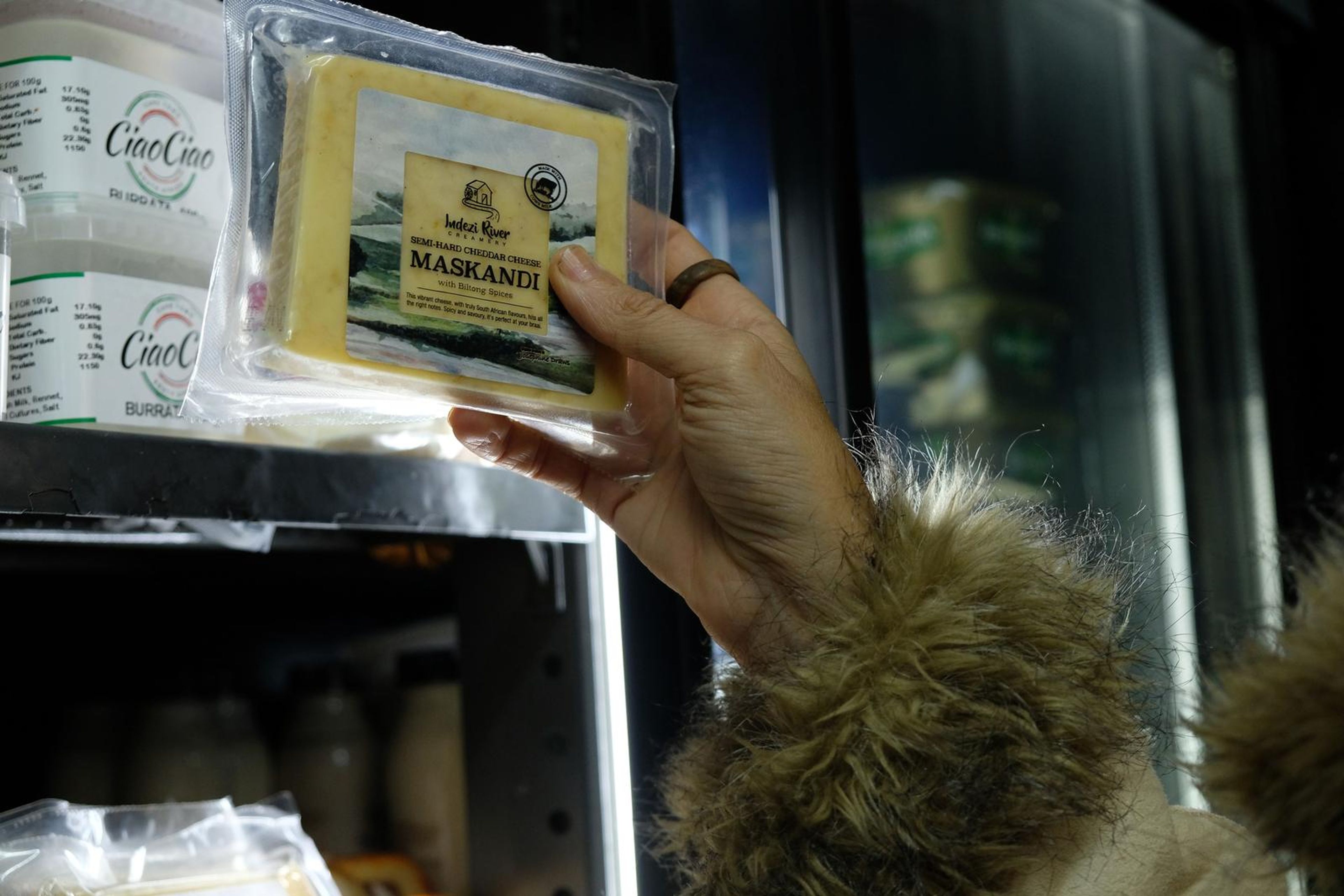 Hands holding a pack of Maskandi cheese beside the fridge