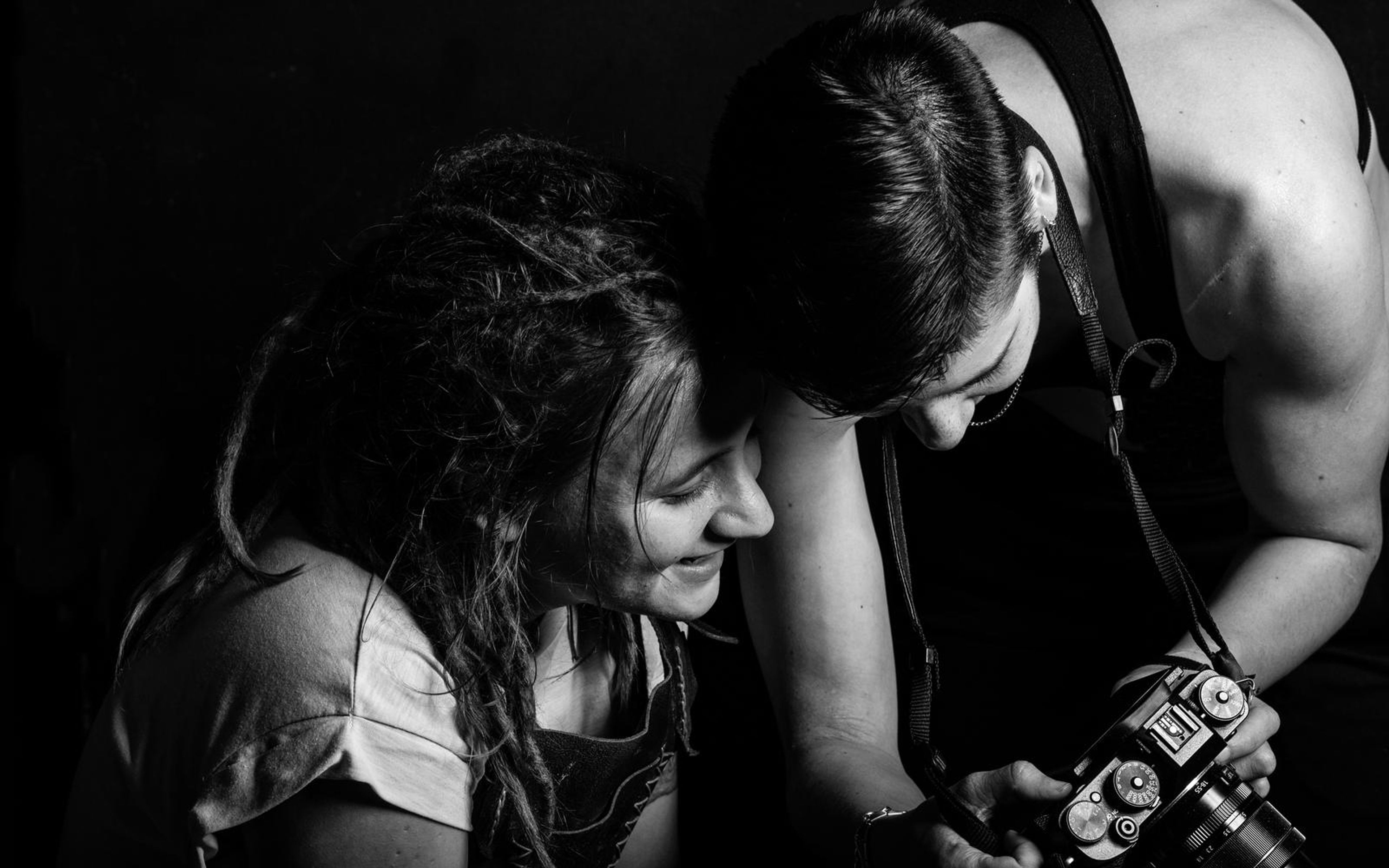Black and white behind the scenes shot of a photographer holding a camera and showing a dreadlocked woman the screen