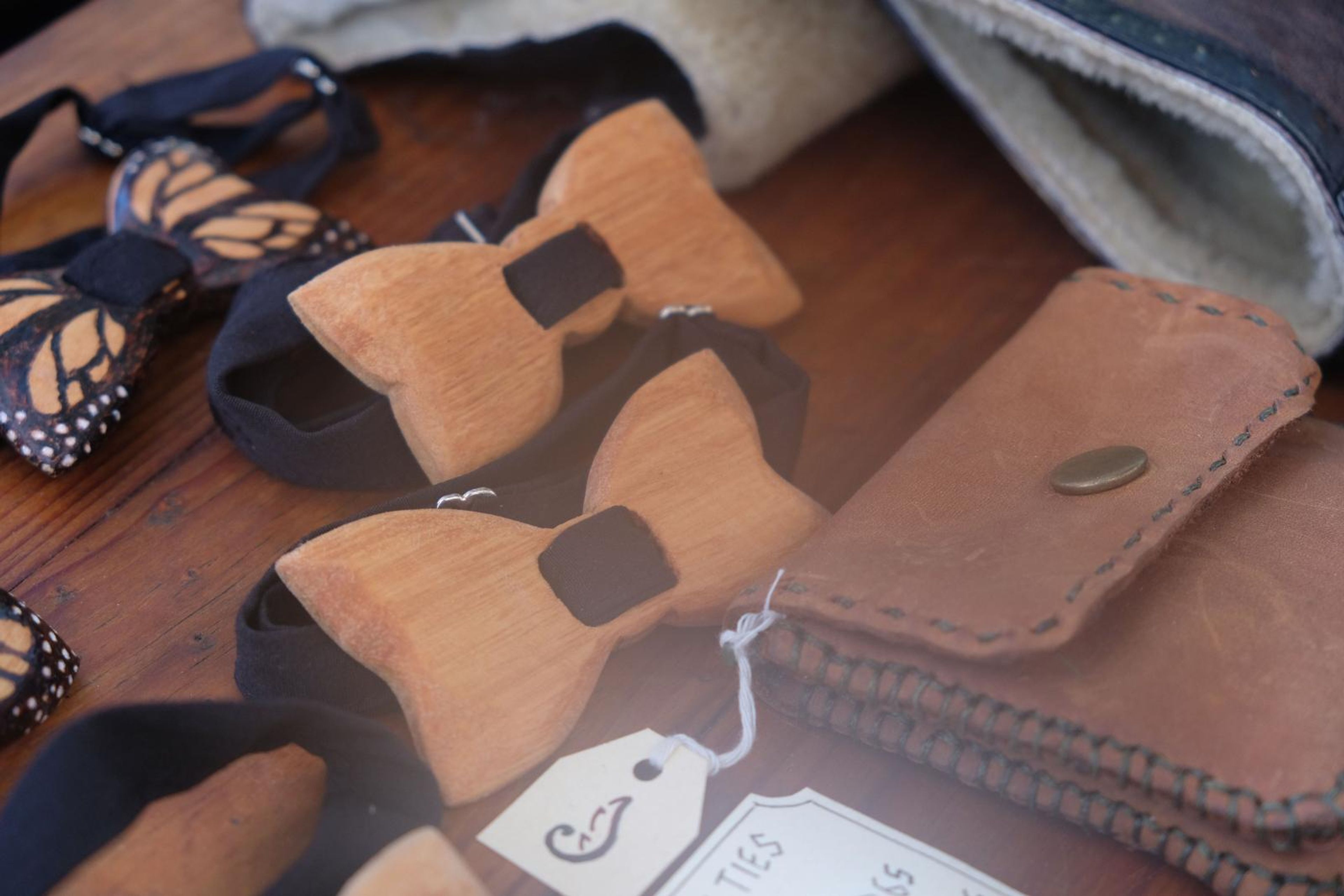 Carved wooden bow ties and tan leather pouches on the table