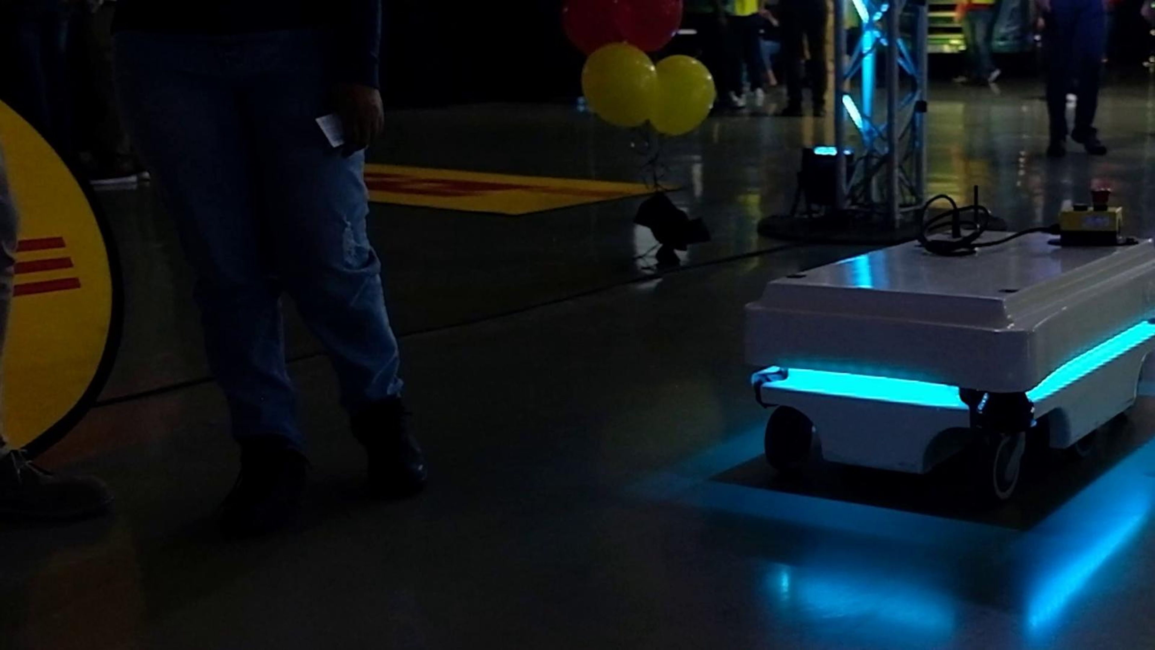 Autonomous robot gliding between stands under cyan light