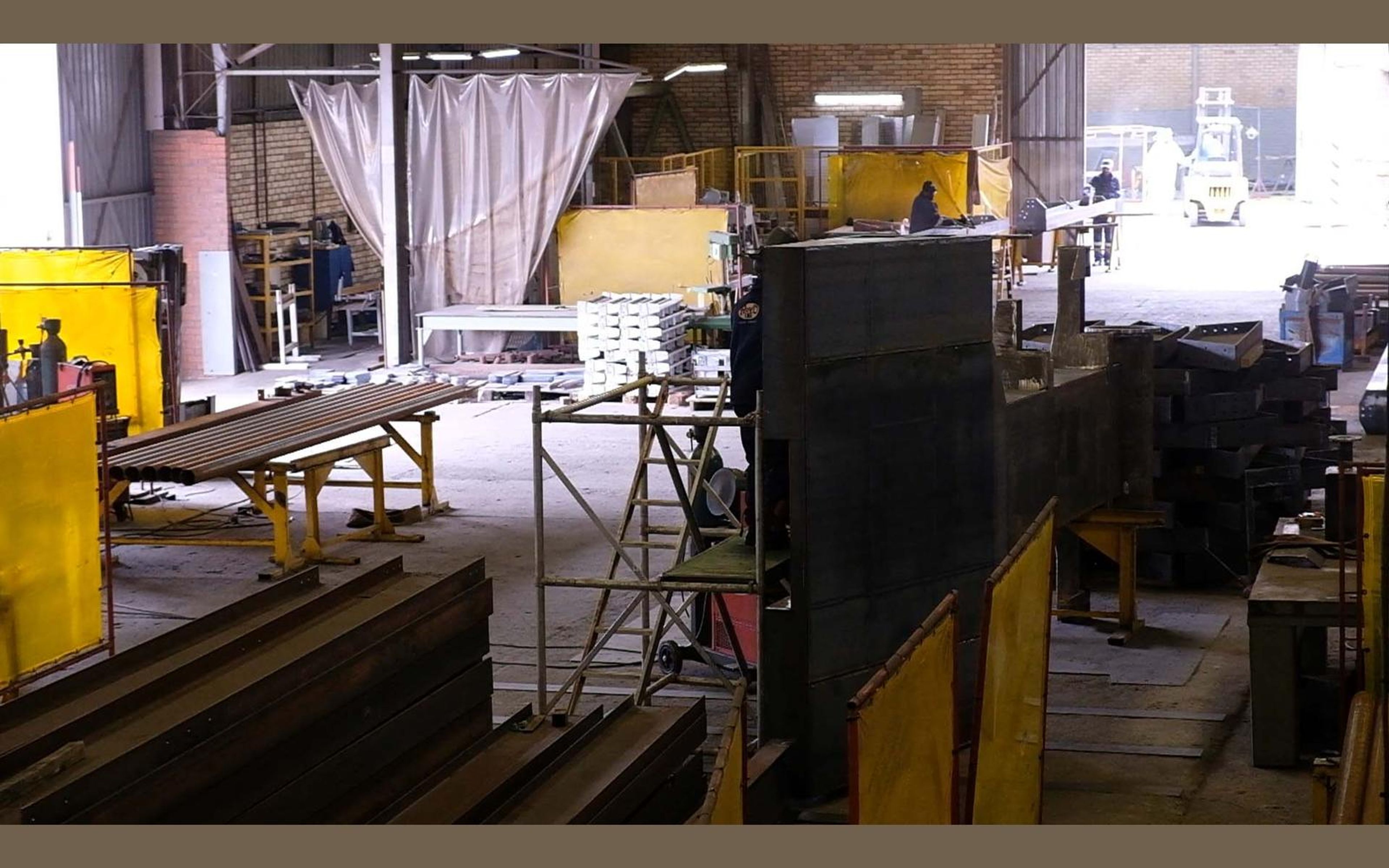 Fabrication bay with yellow welding screens and steel sections