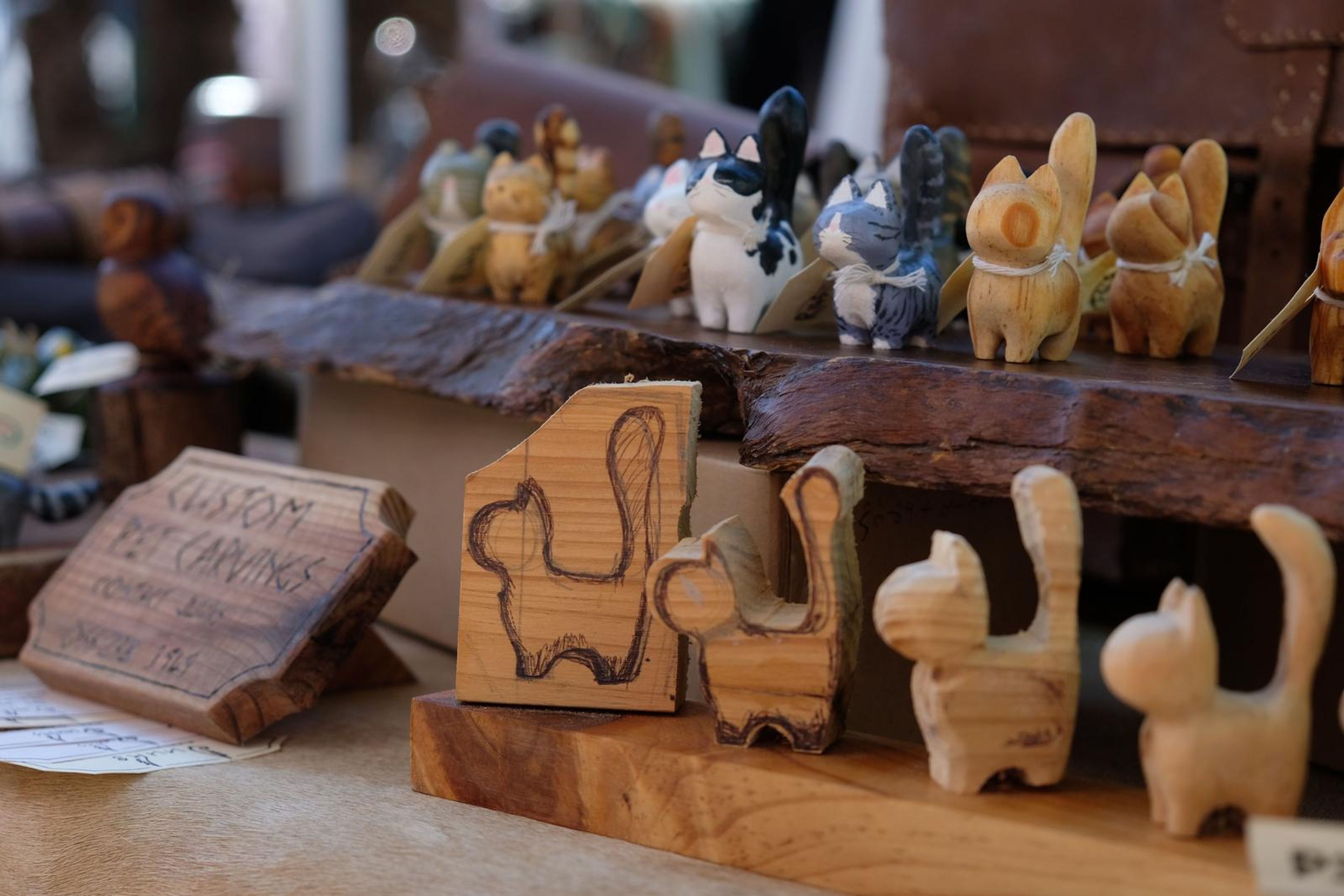 Hand-carved wooden cats on a bark shelf beside a leather satchel