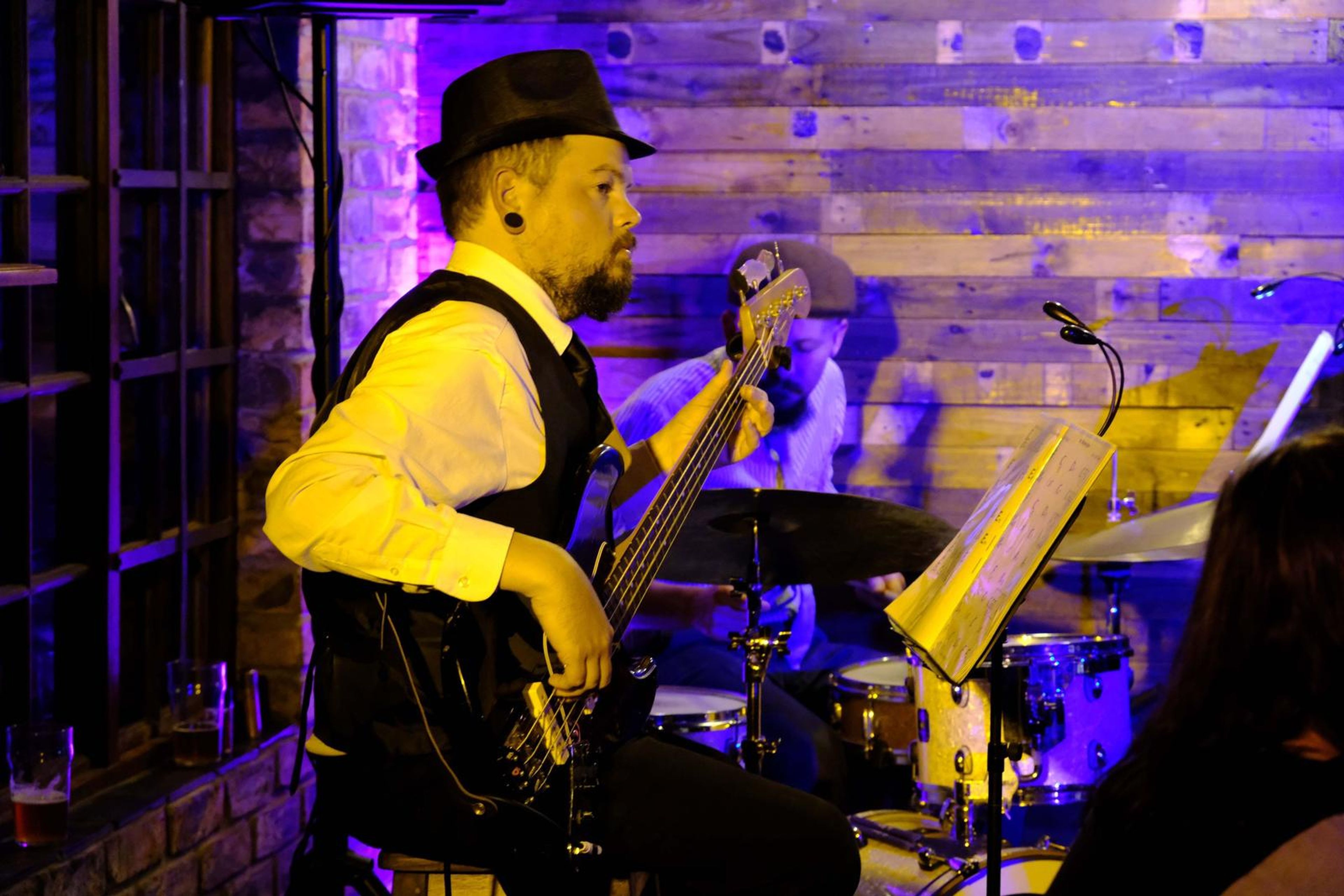 Bassist in a hat playing with the drummer behind him