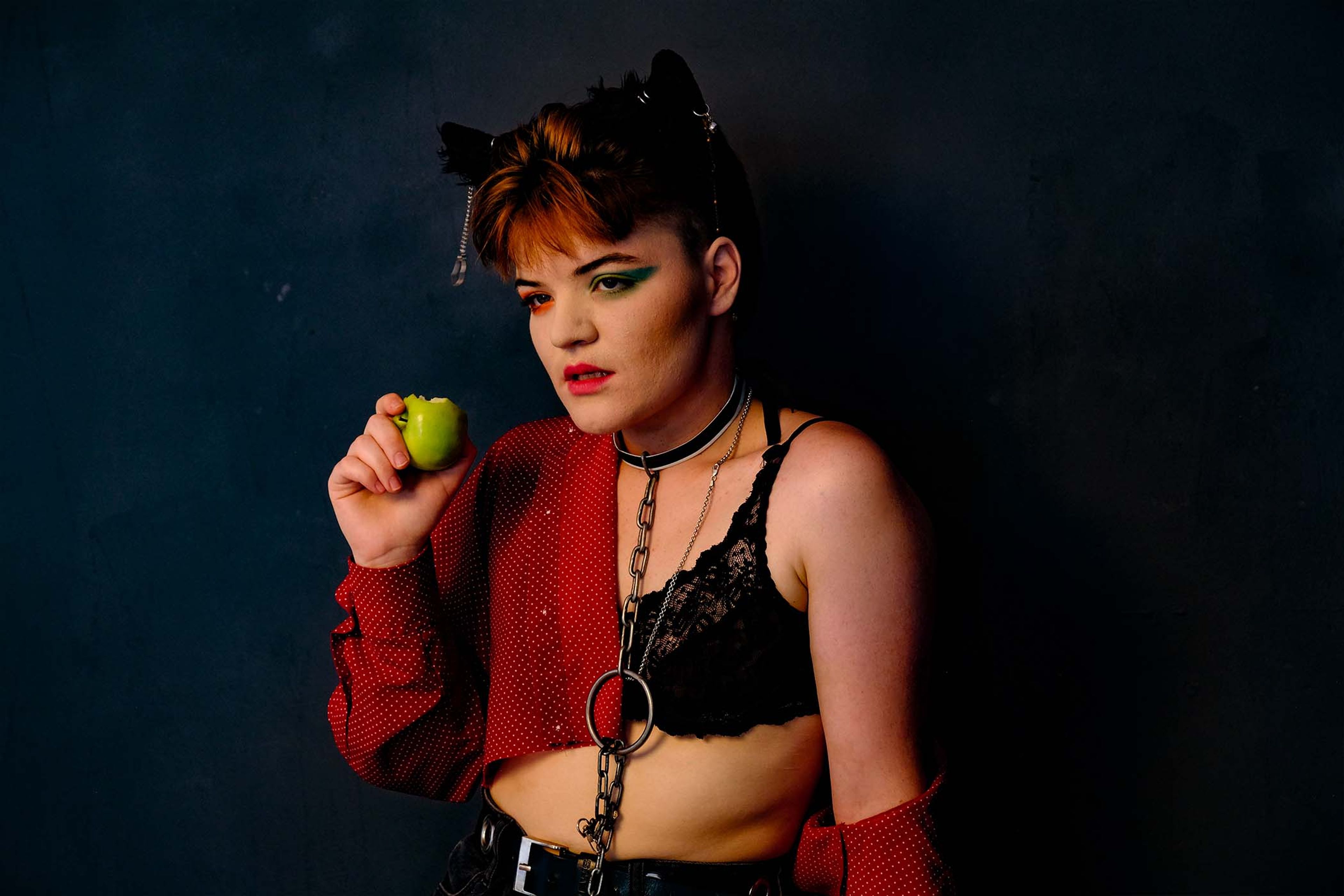 Portrait, subject in a lace bra and cat-ear headpiece holding a lime, chain choker visible
