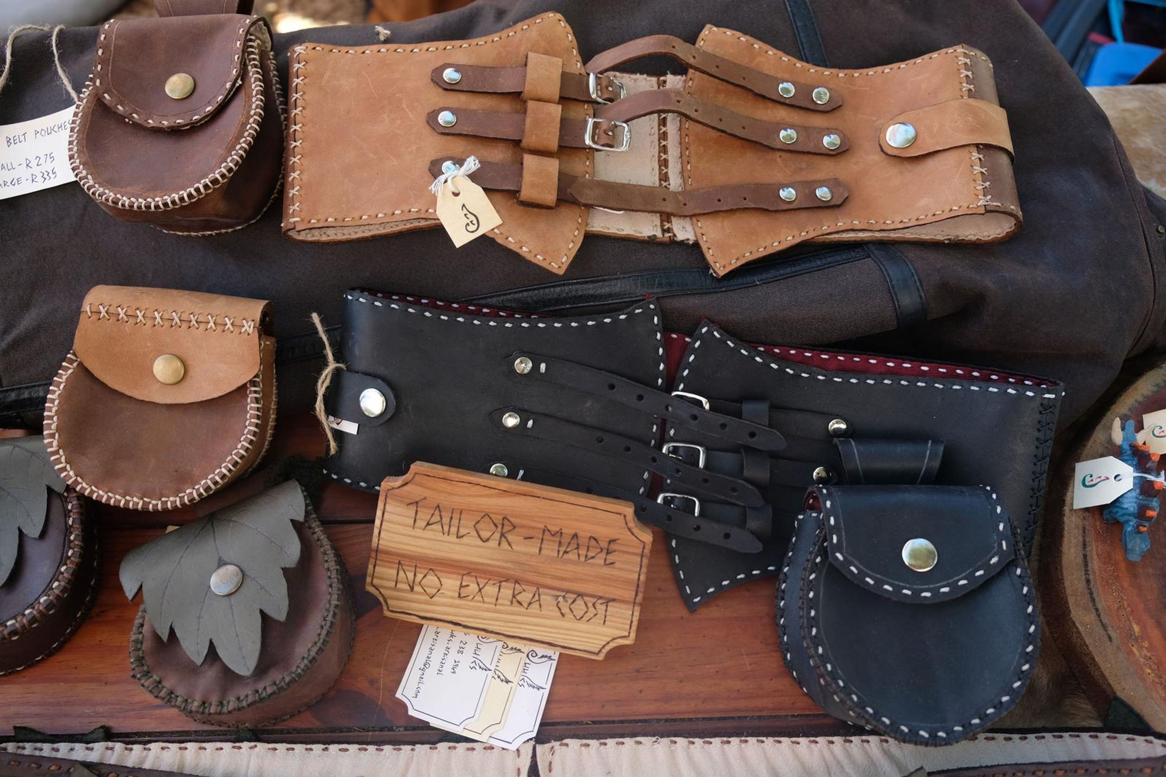 Table of handmade leather pouches and corset belts with a Tailor-Made sign