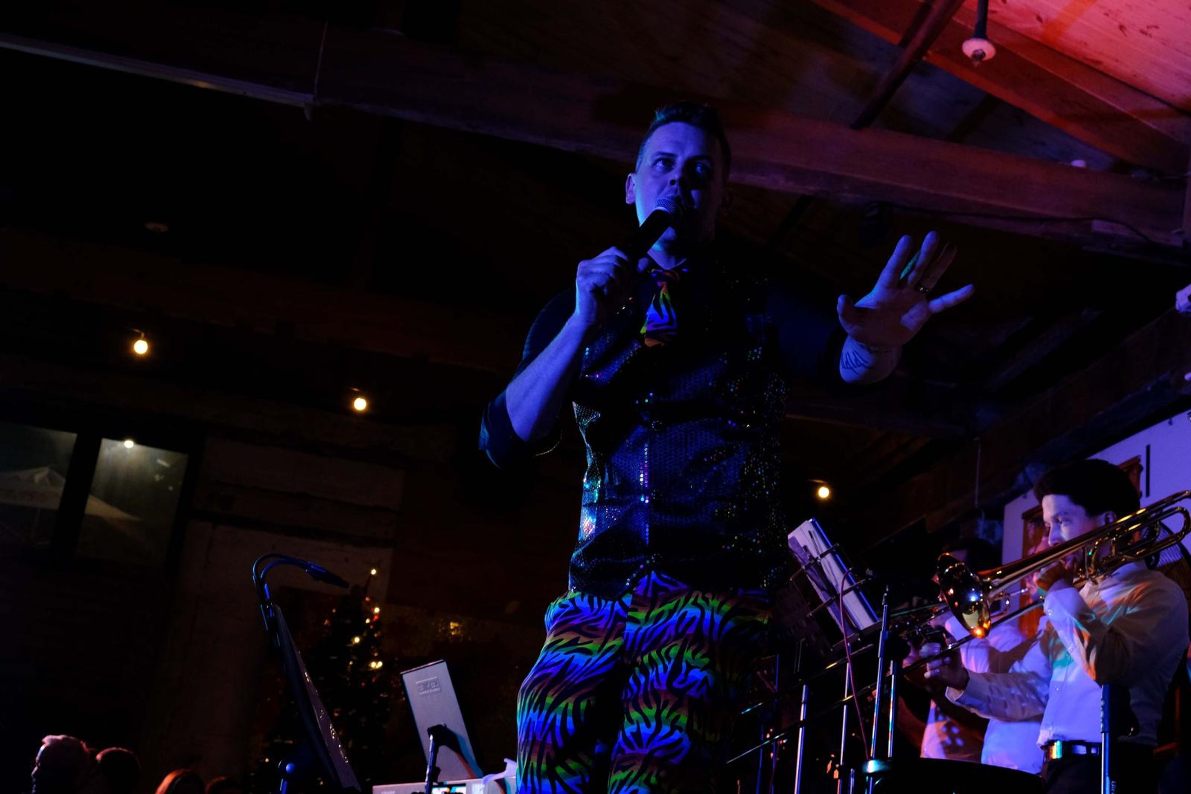 Singer in a black waistcoat and rainbow trousers singing on stage