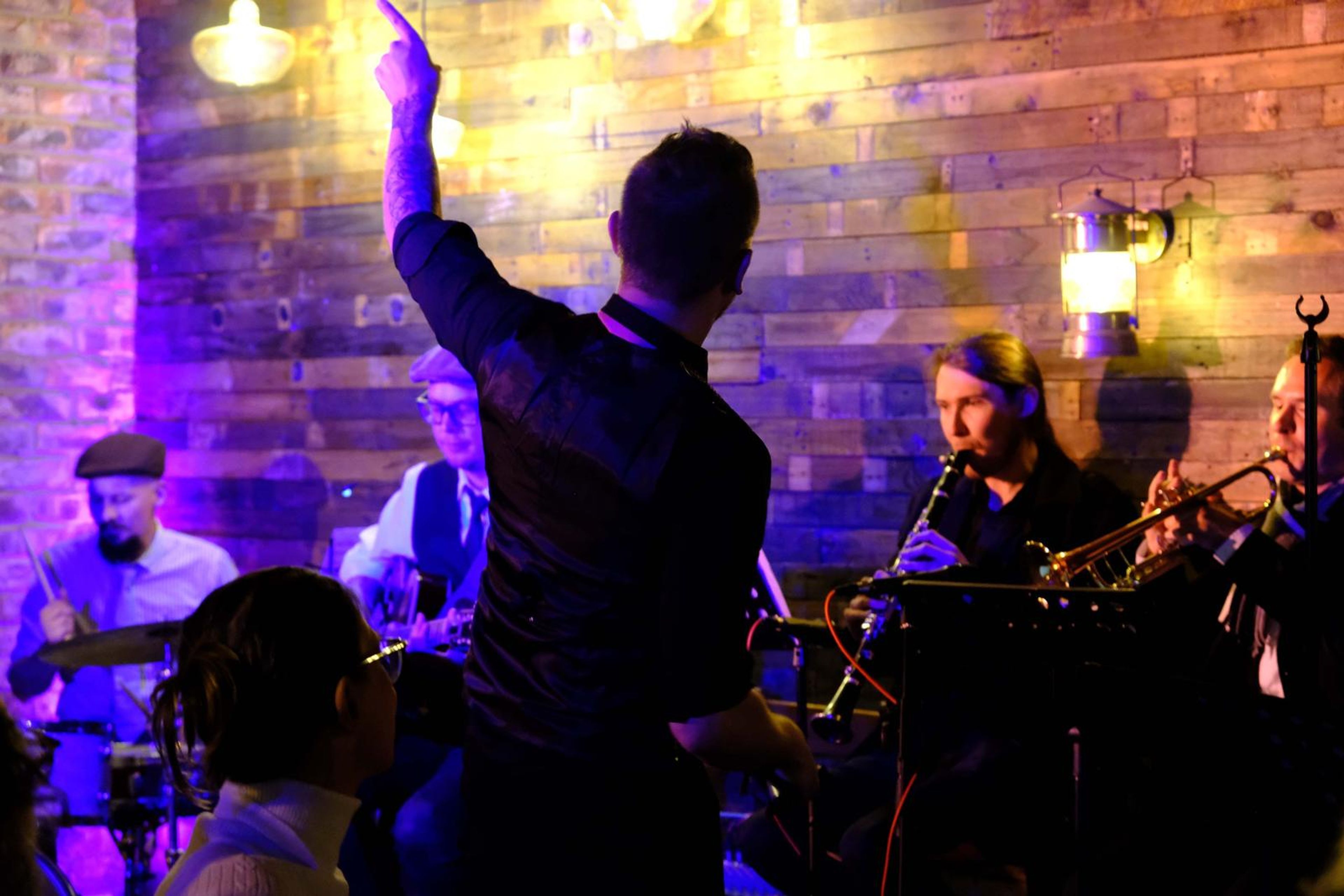 Lead singer with his arm raised, seen from behind, in front of the band