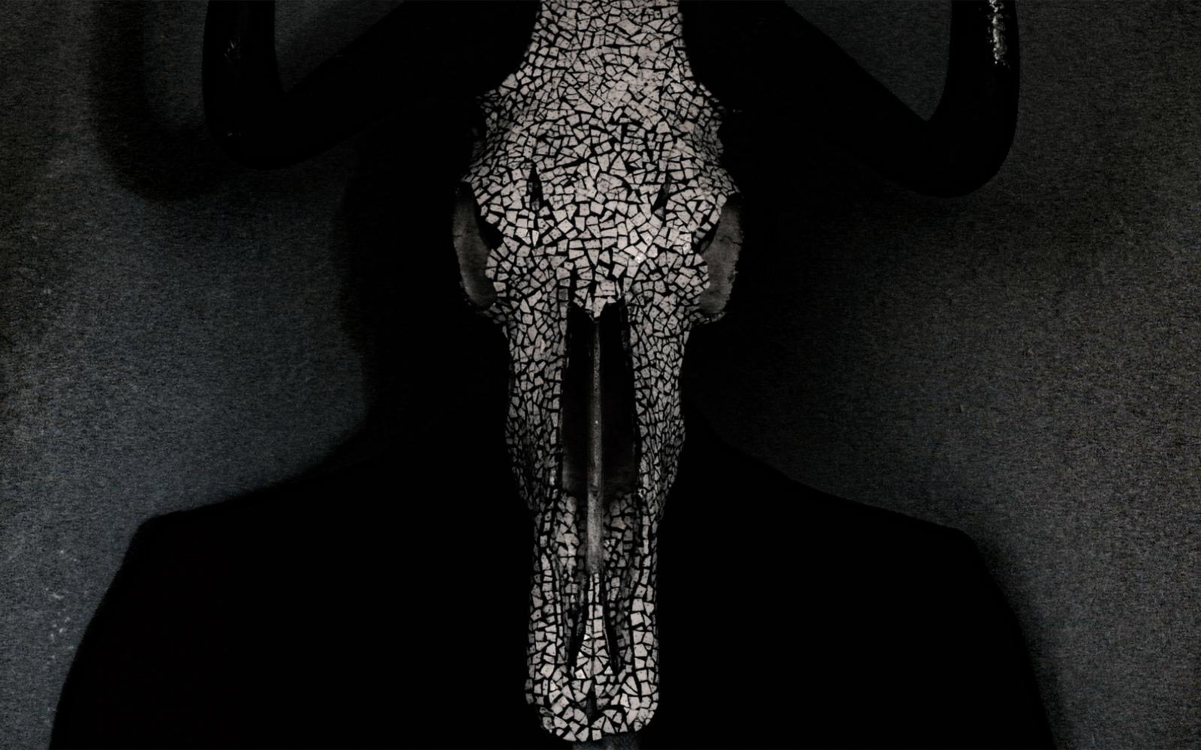 Horned skull covered in cracked white mosaic fragments, held in front of a person in a dark jacket against a grey backdrop