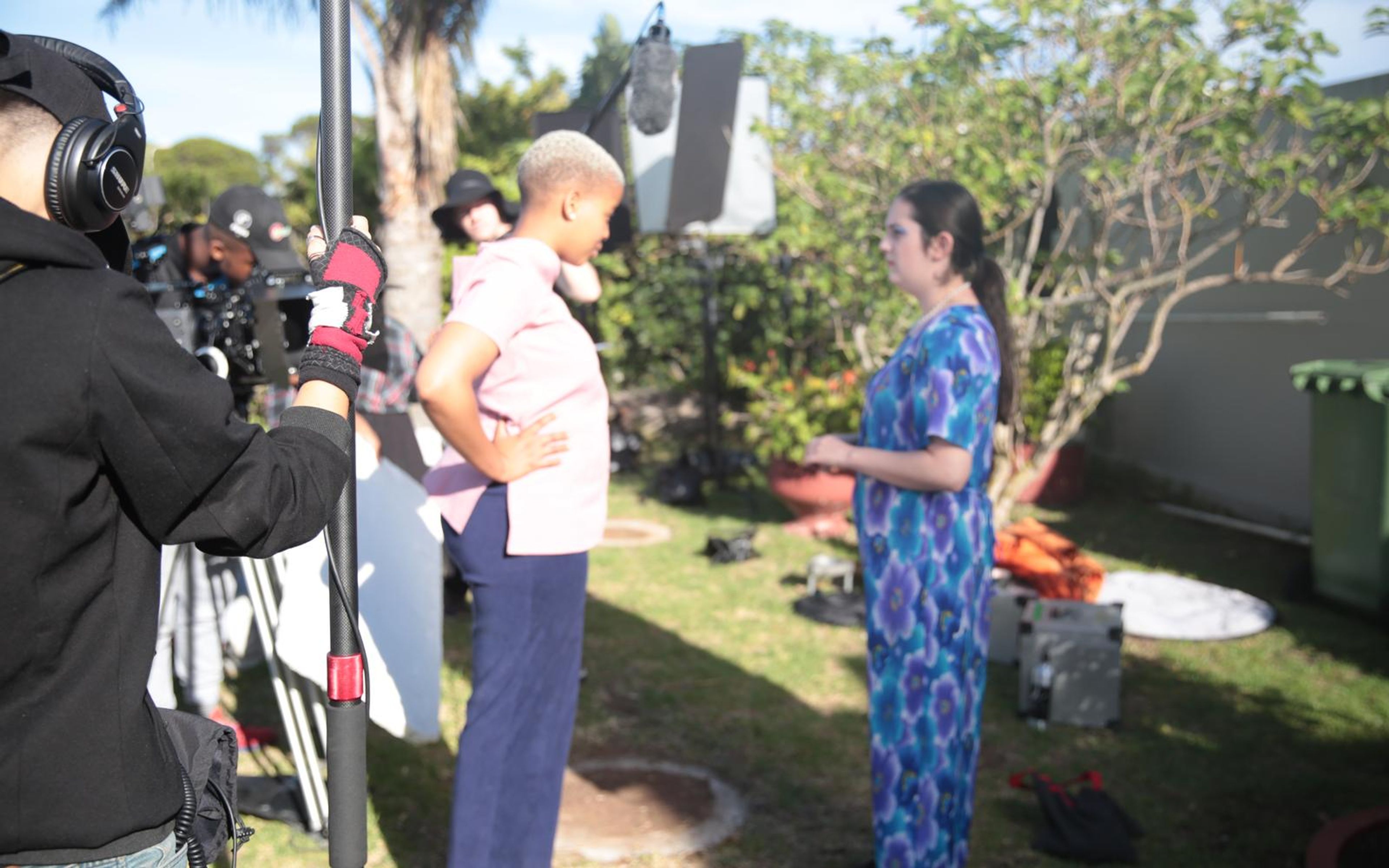Two actors in a garden listening to directions while a camera operator and boom operator in headphones stand ready