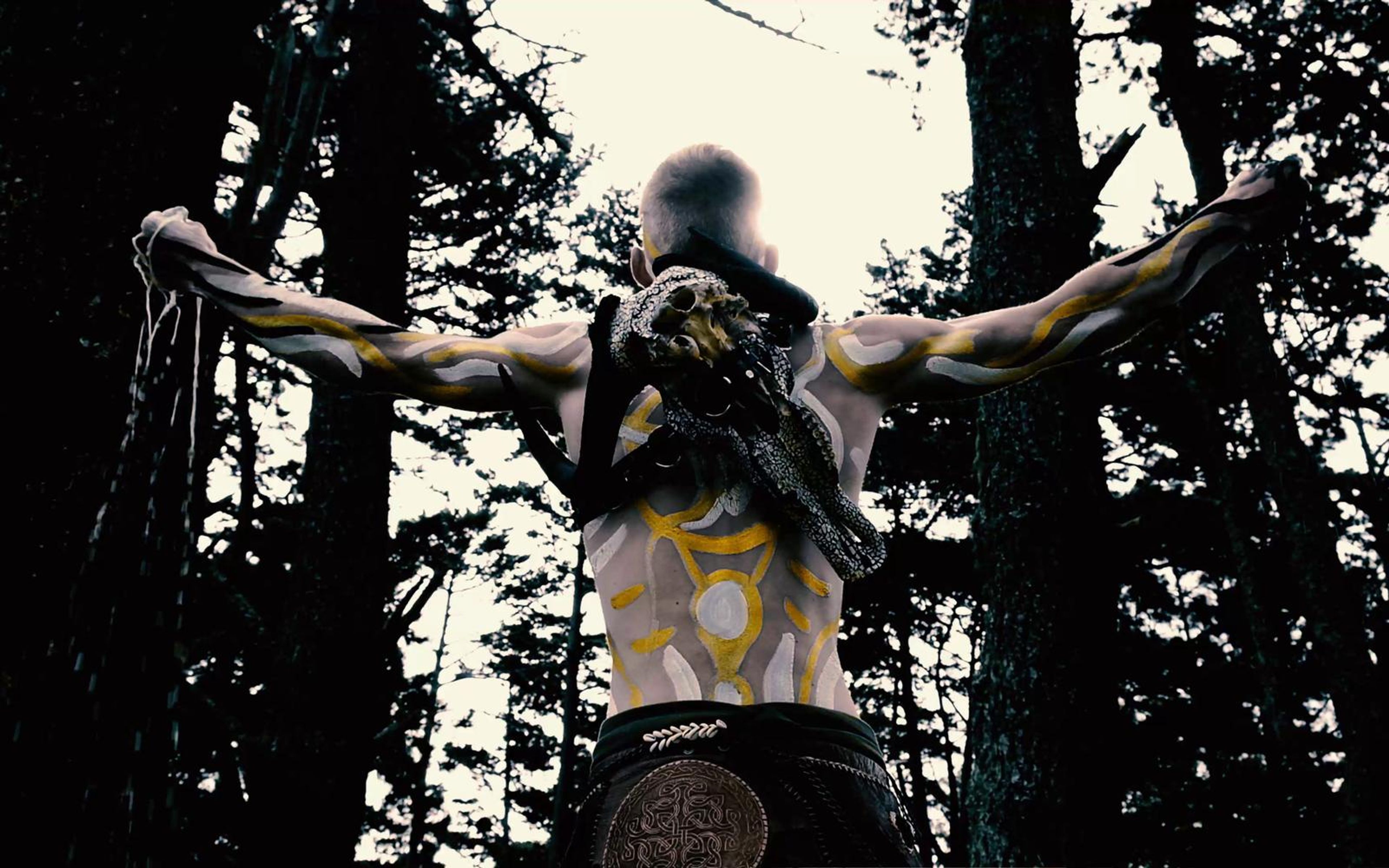 Performer from behind with arms outstretched and a skull strapped to his back, high contrast