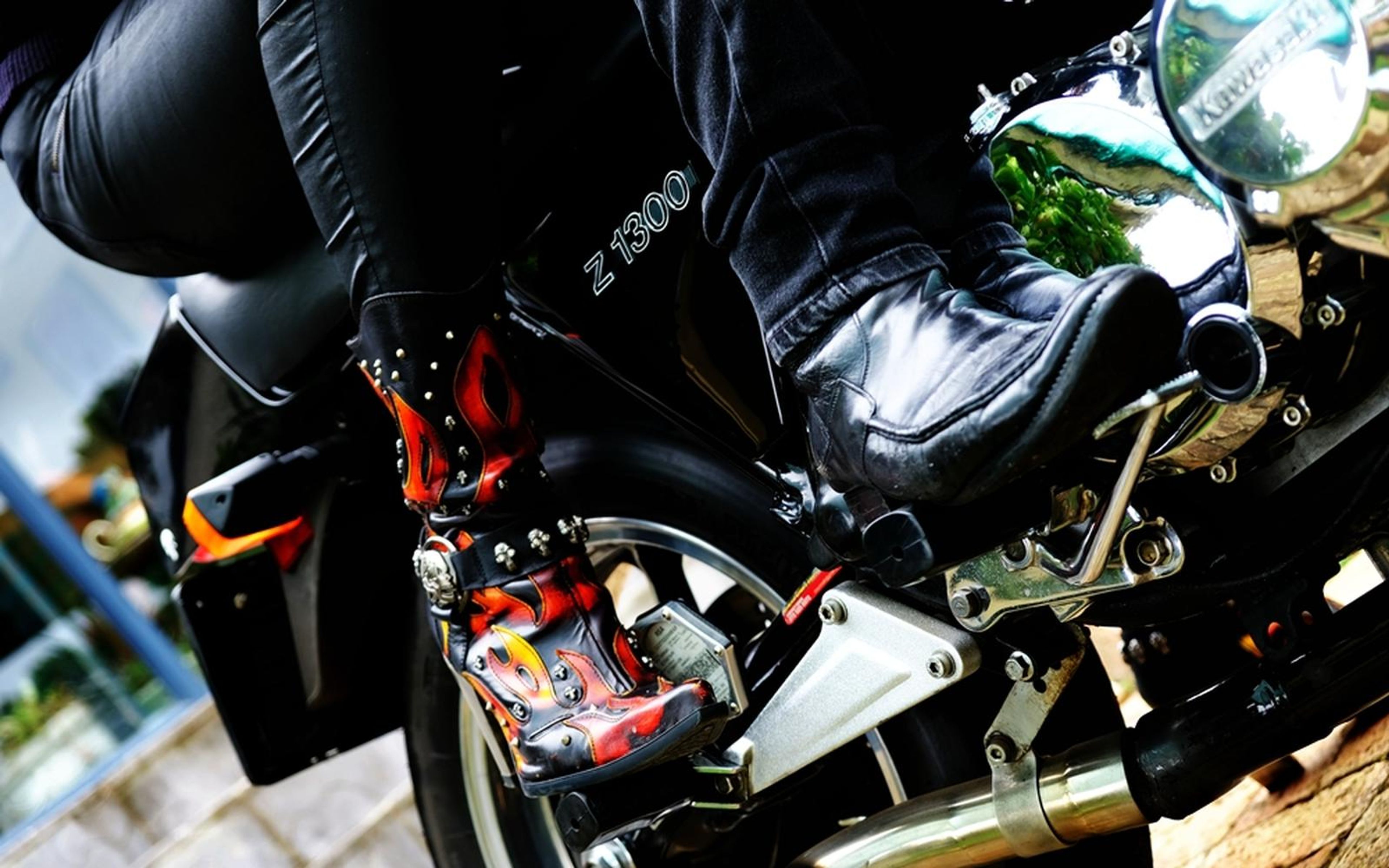 Low angle on a rider's black boot with a flame design resting on a motorbike footrest