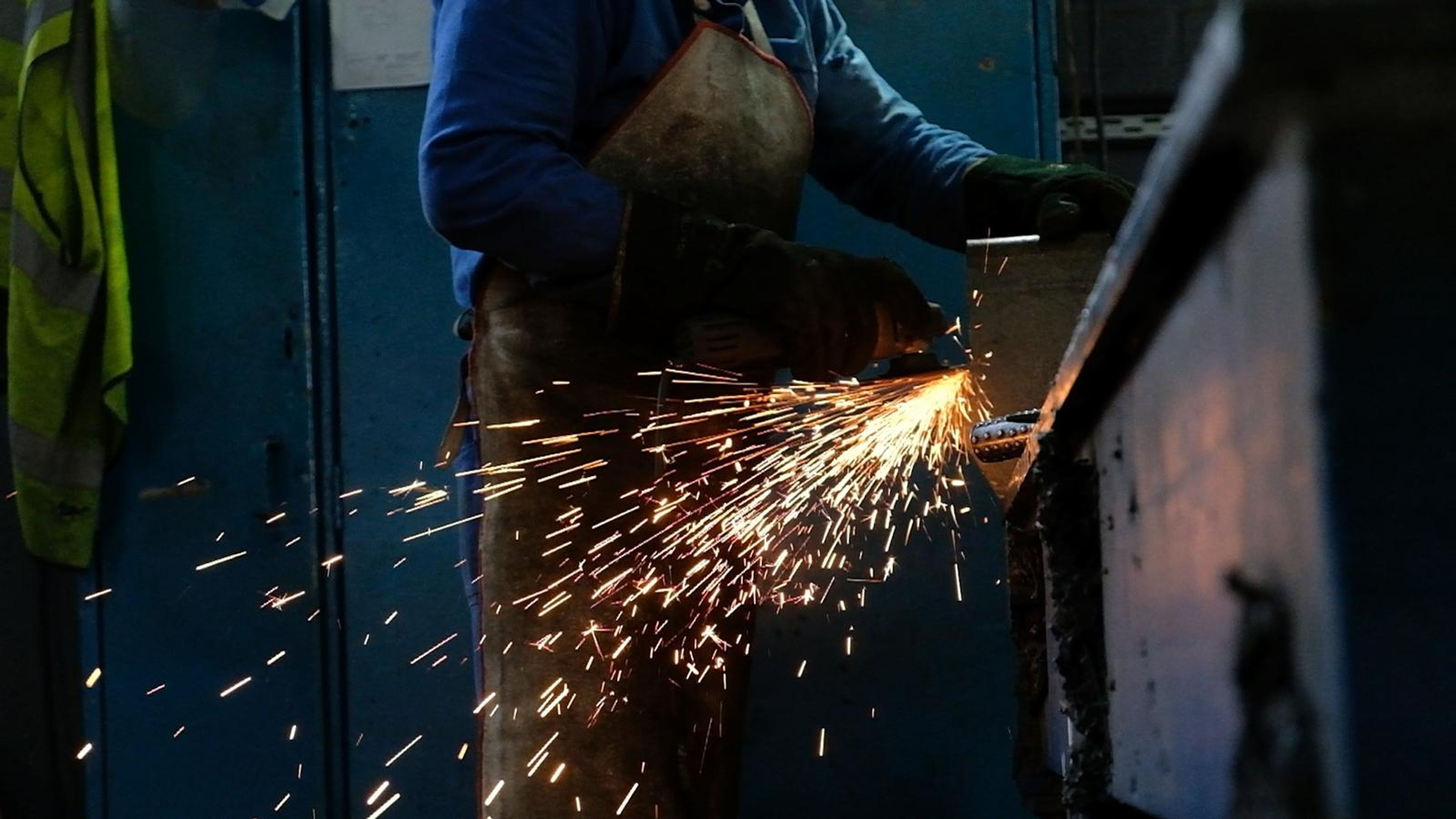 Worker in an apron grinding a steel edge in a shower of sparks