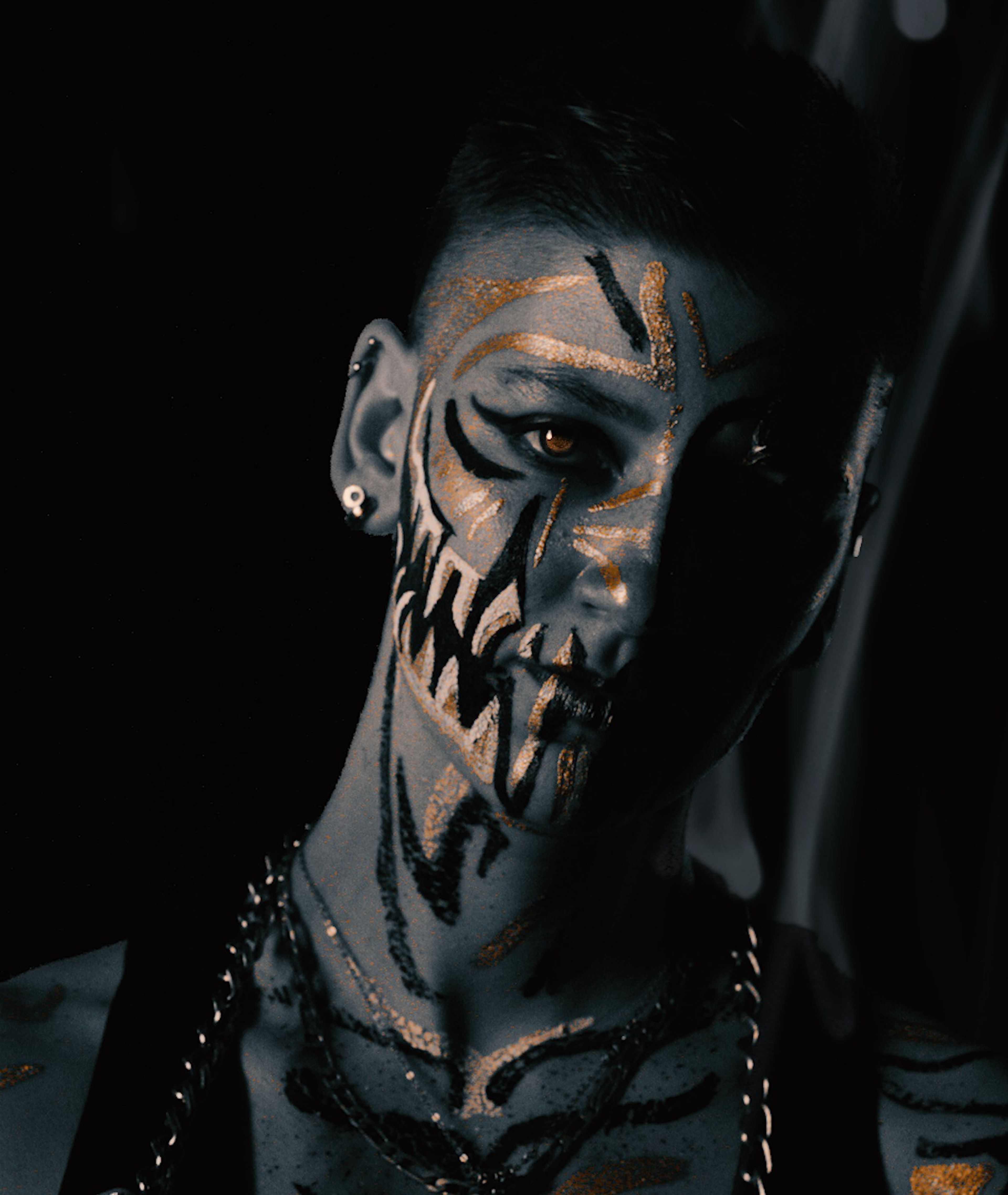 Face-painted portrait with black fang markings, softly lit with a dark curtain behind