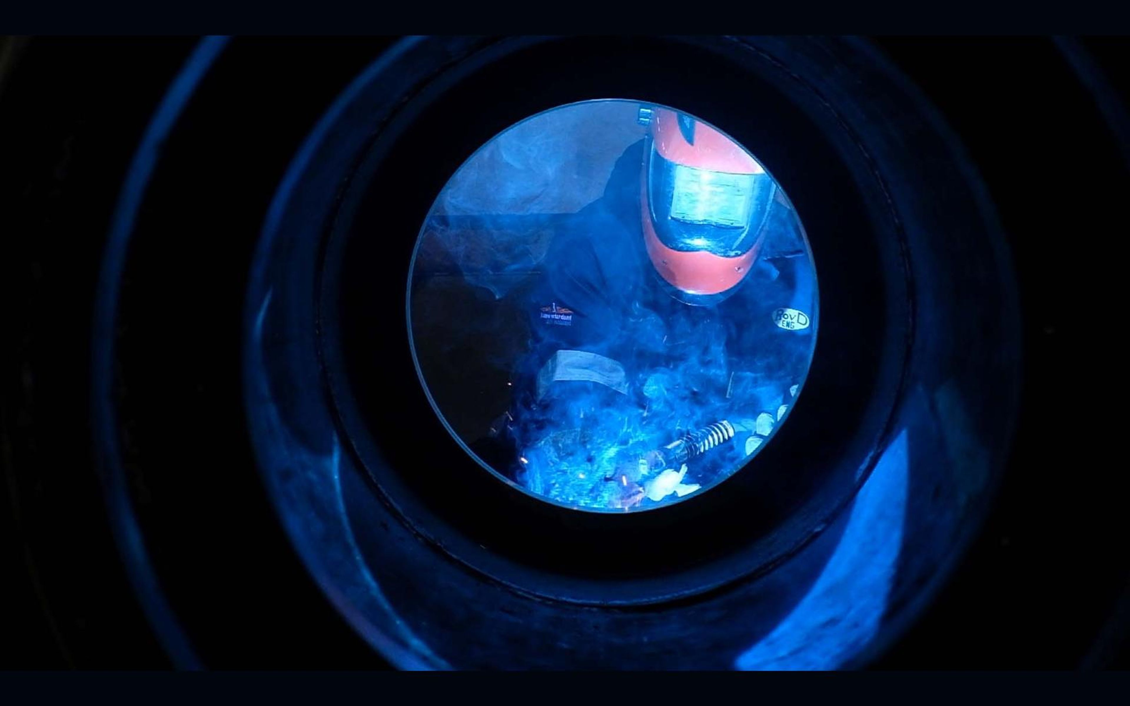 Welder seen through a round steel opening