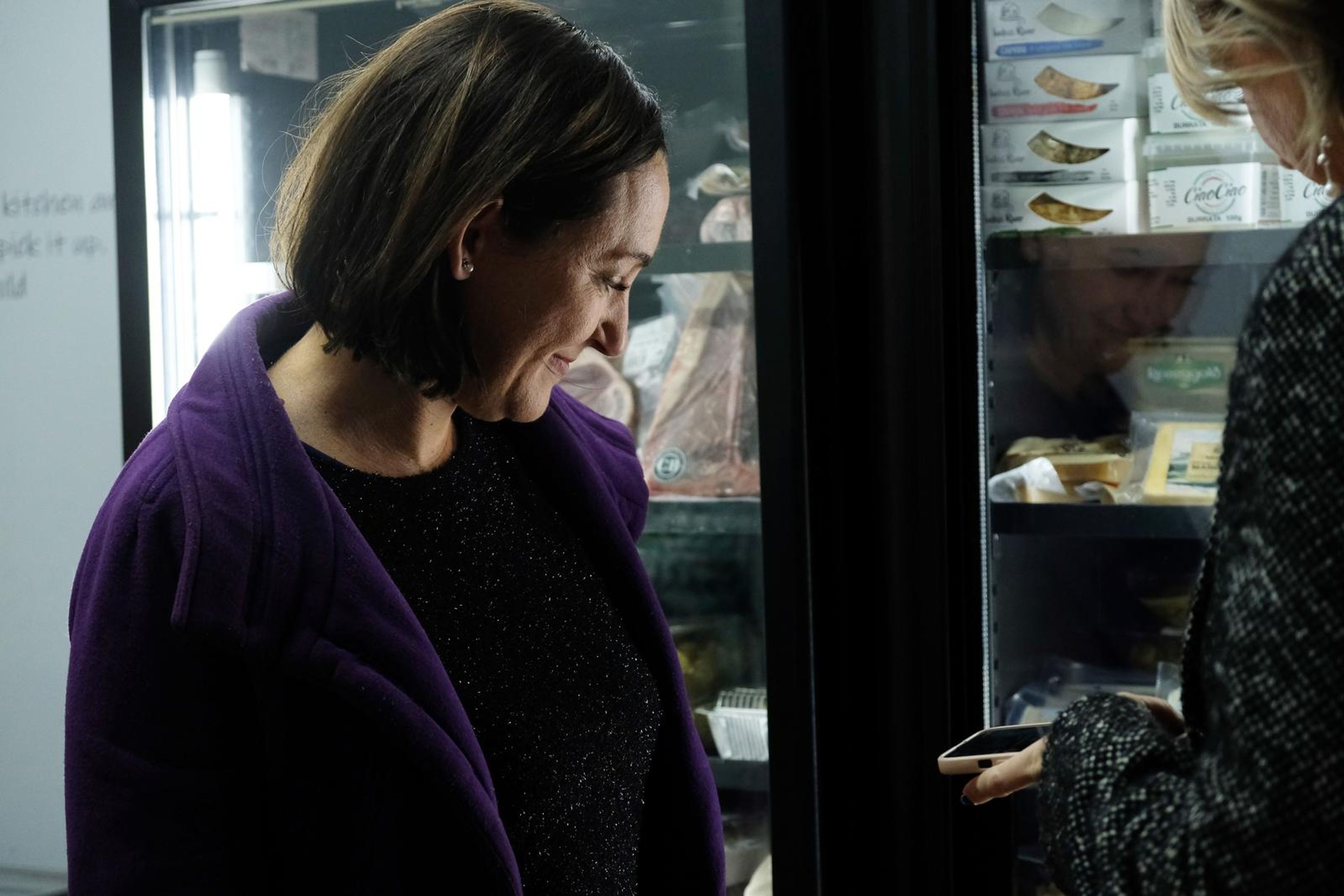 Guest in a purple coat looking down at her phone beside the fridge