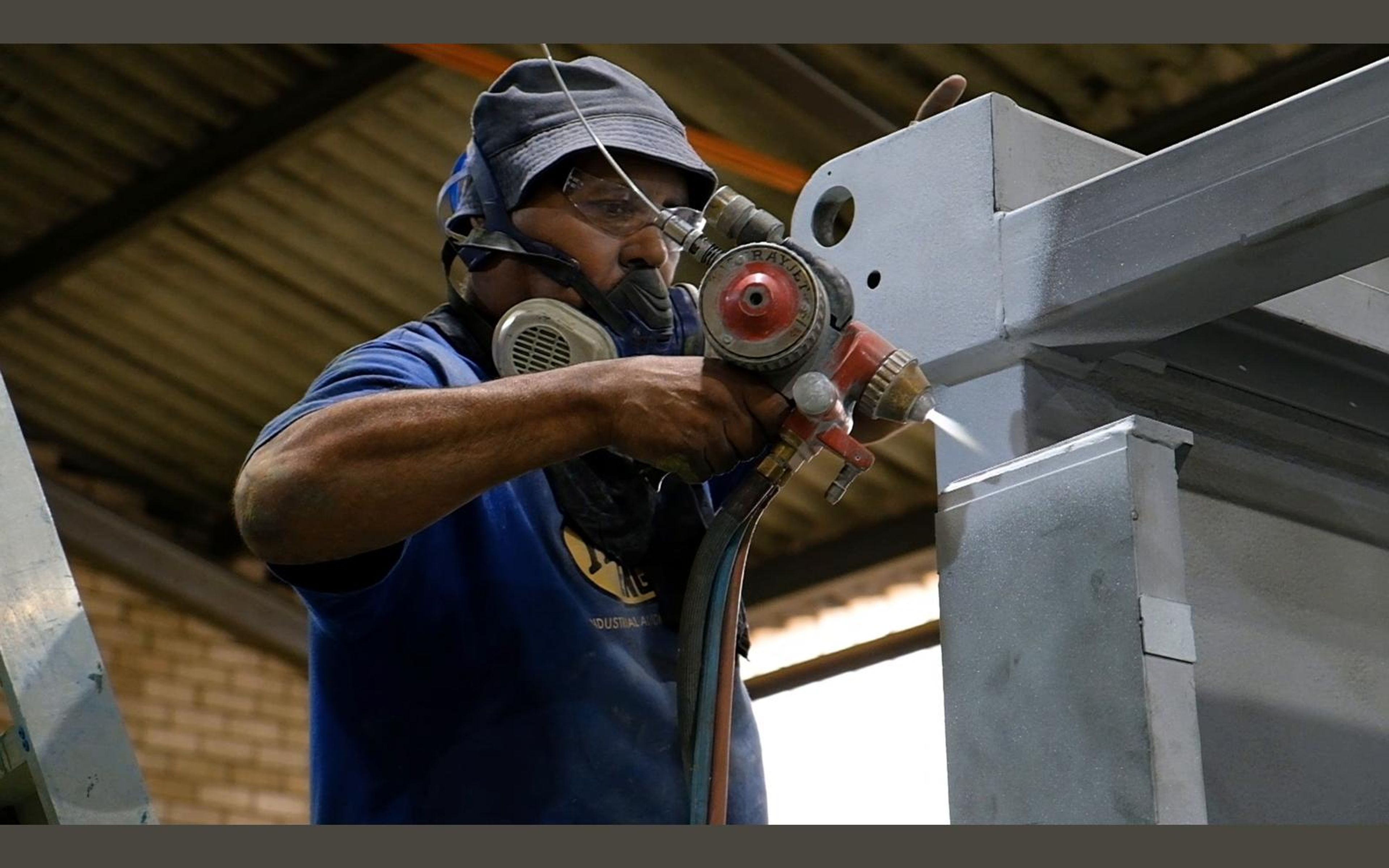 Painter in a respirator spraying a steel part