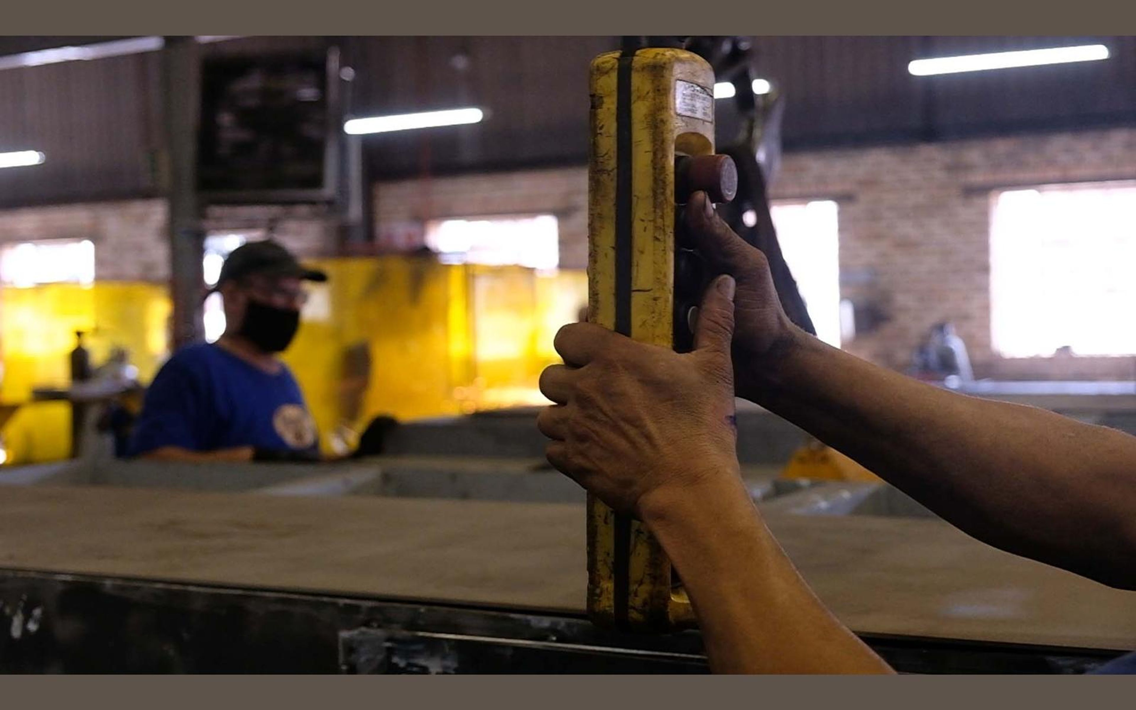 Worker holding a steel part against a yellow screen