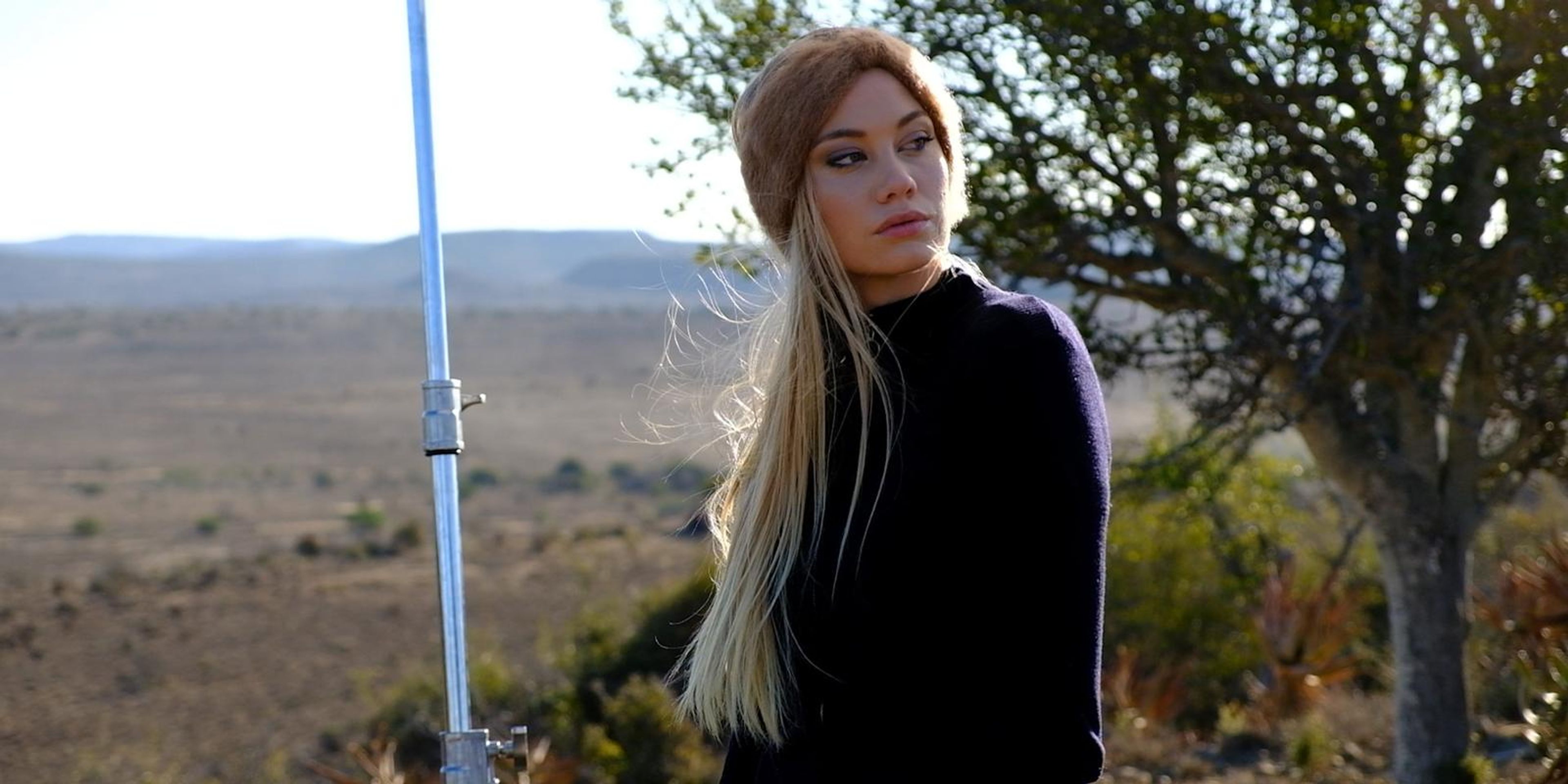 Model with long blonde hair in a dark knit, looking over her shoulder