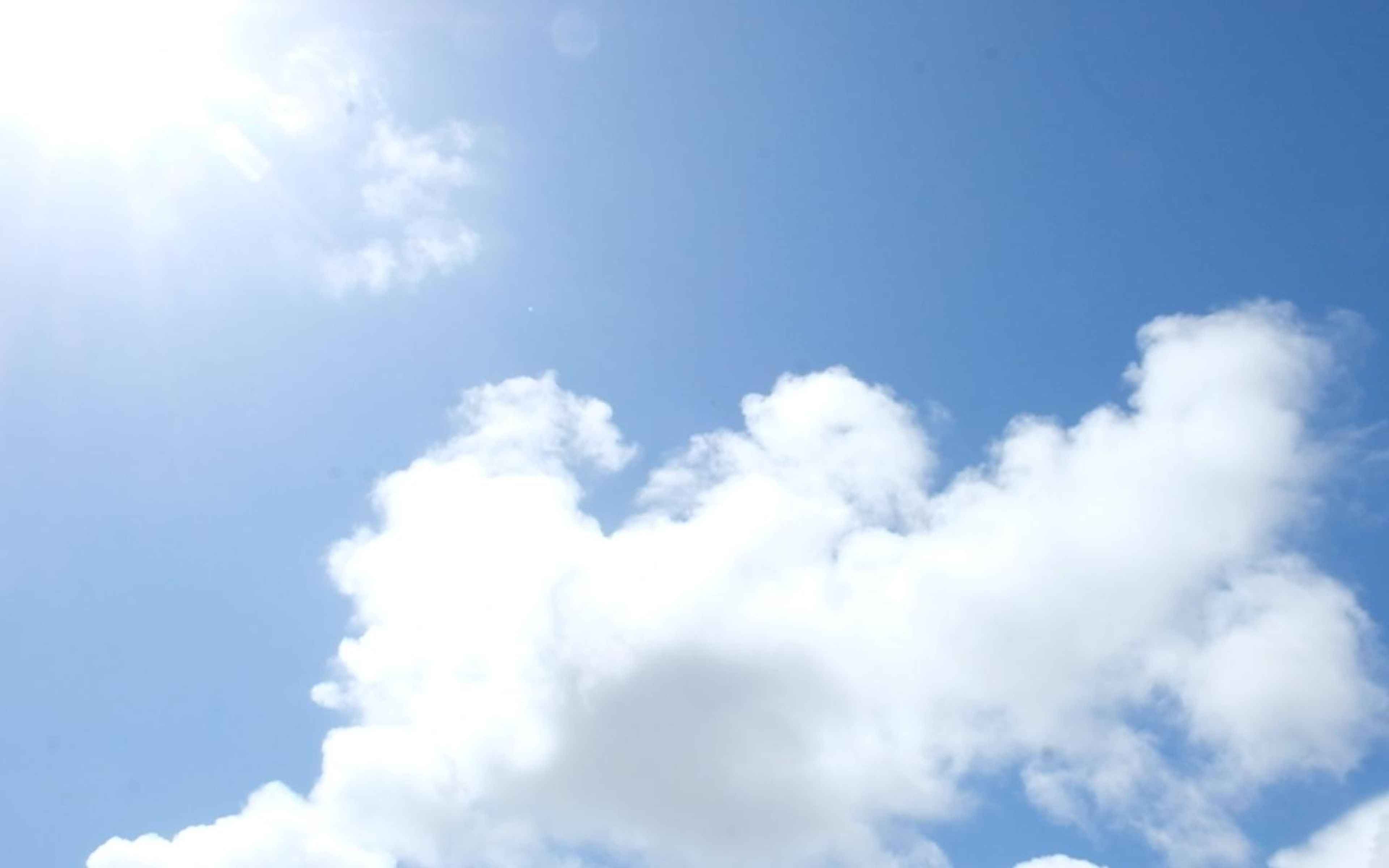 White cumulus clouds in blue sky with the sun at upper left