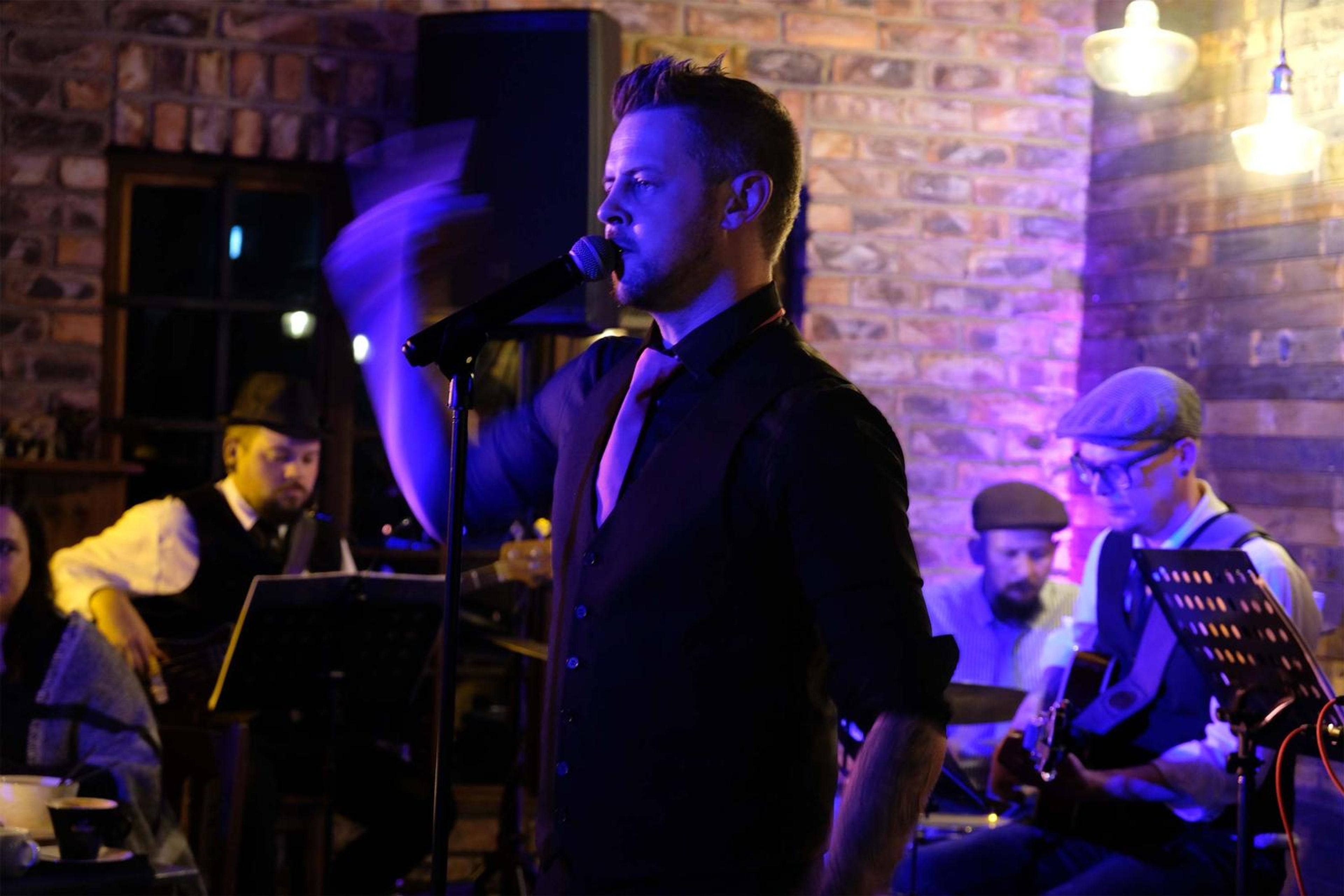 Lead singer in a black shirt performing with the band in purple and gold light
