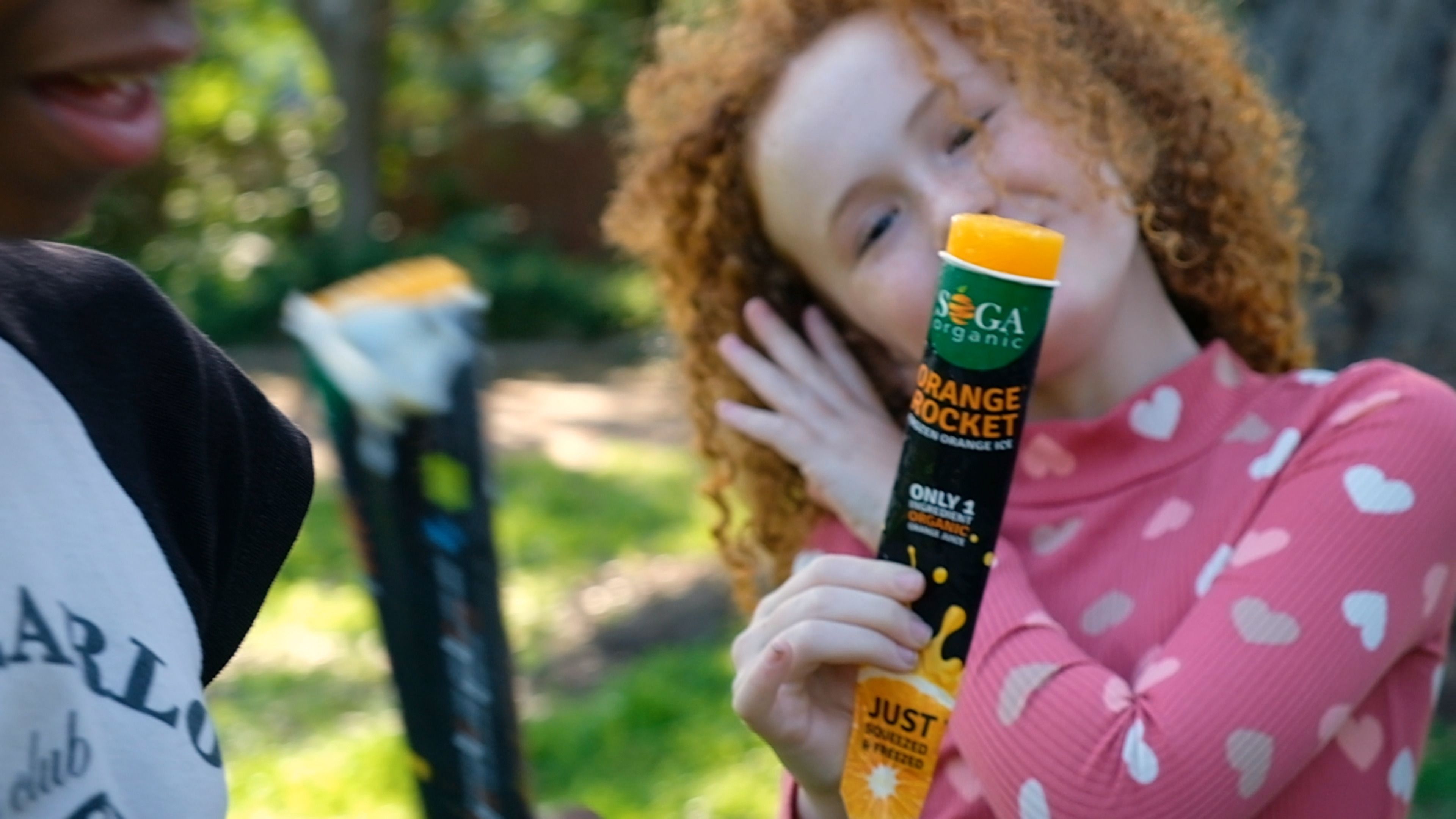 Girl with curly hair smiling and holding an Orange Rocket tube to her face