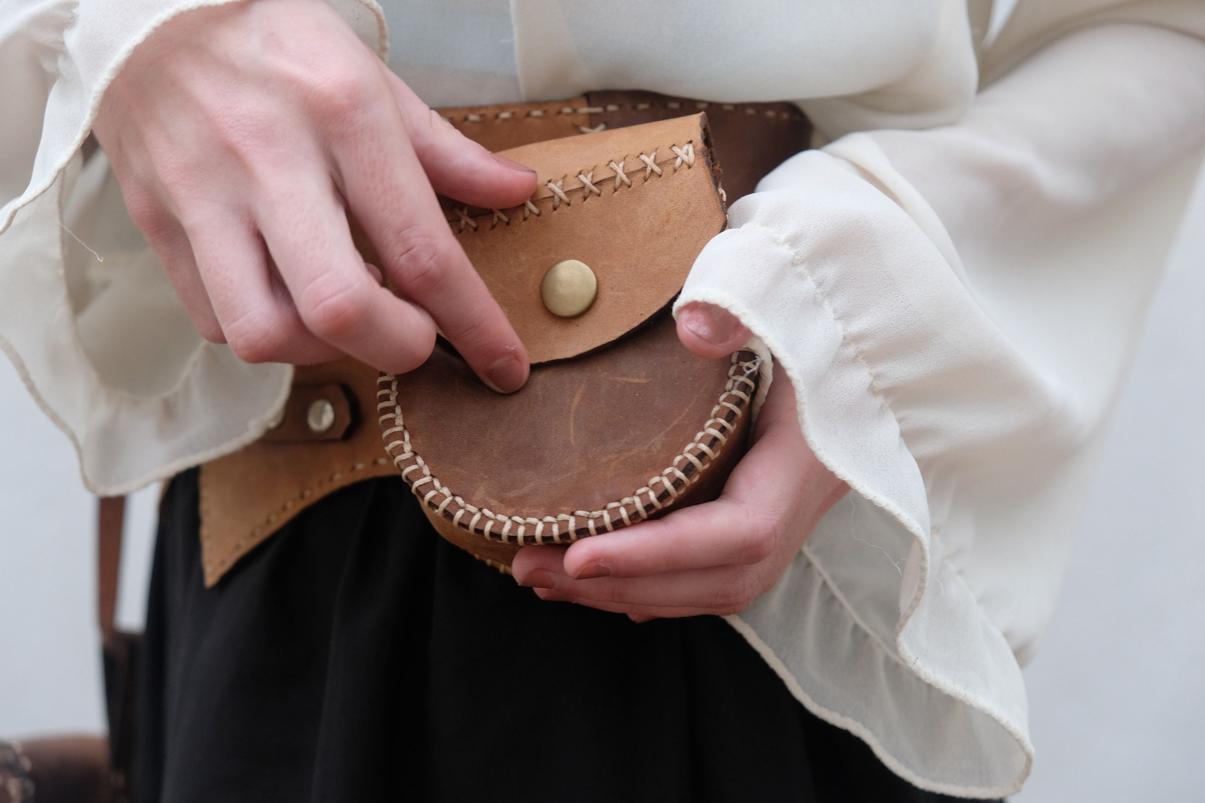 Fingers opening the snap on the round leather pouch