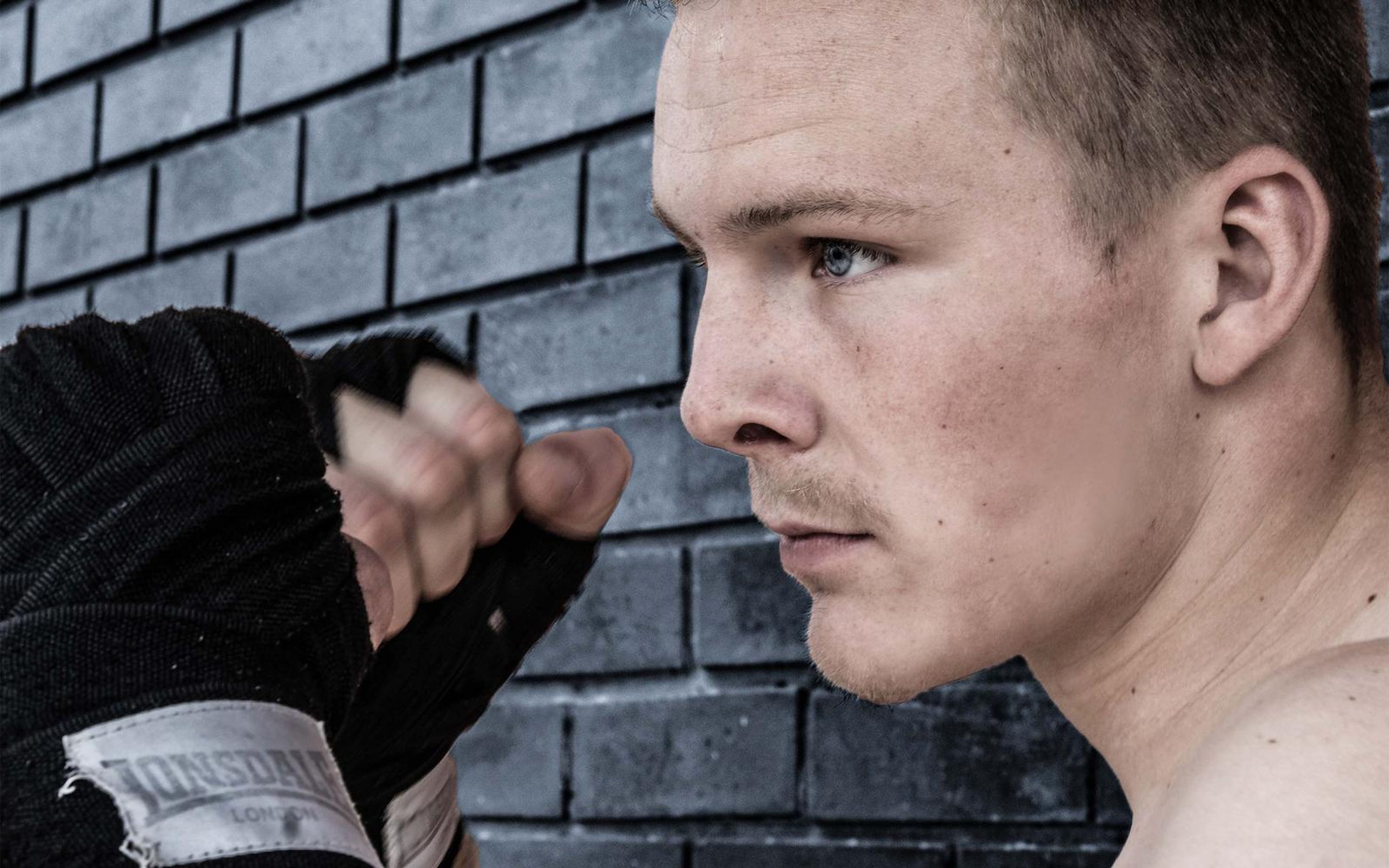 Profile of the fighter with a raised wrapped fist against dark grey brick in cool tones