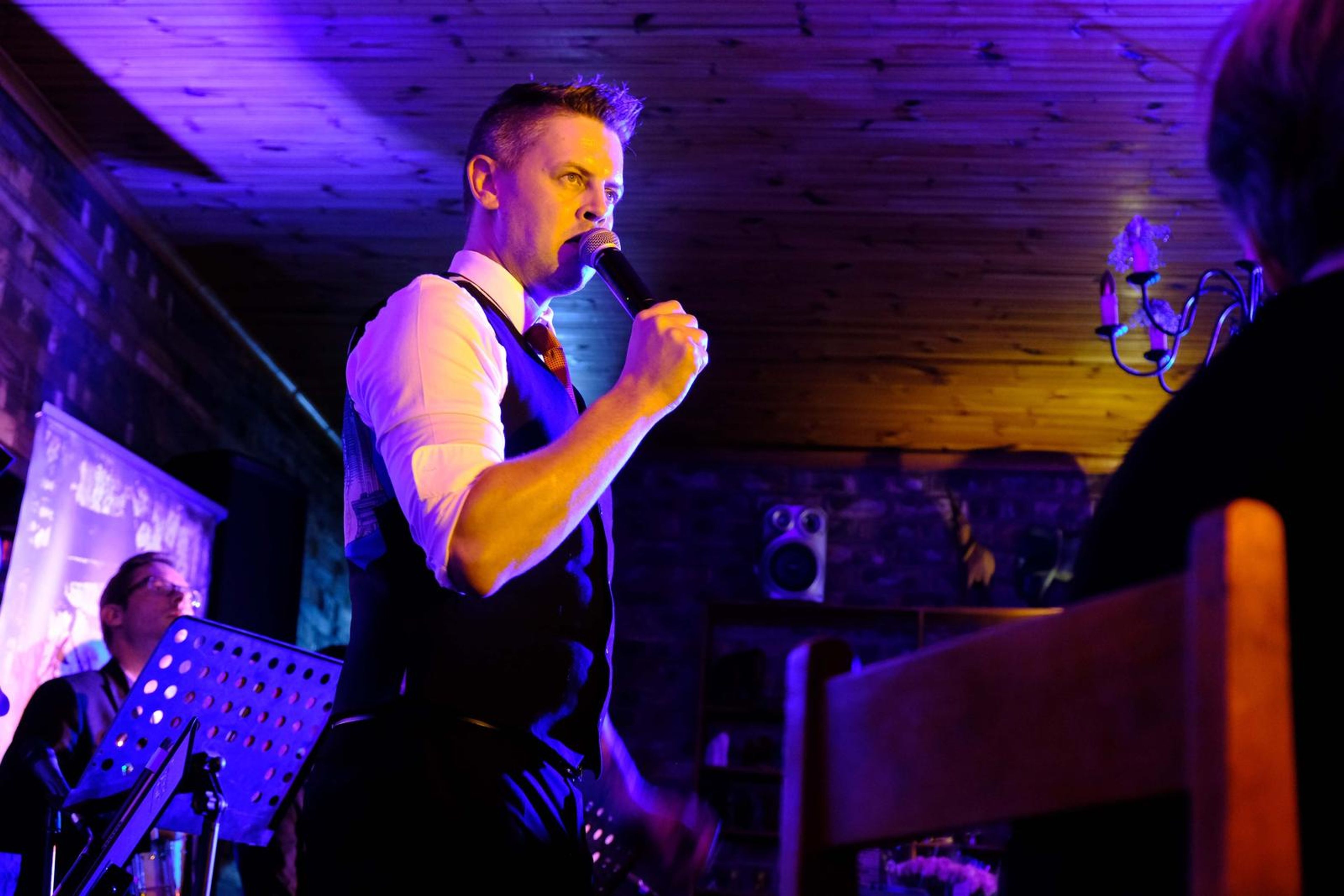 Singer in a waistcoat and rolled sleeves singing between tables