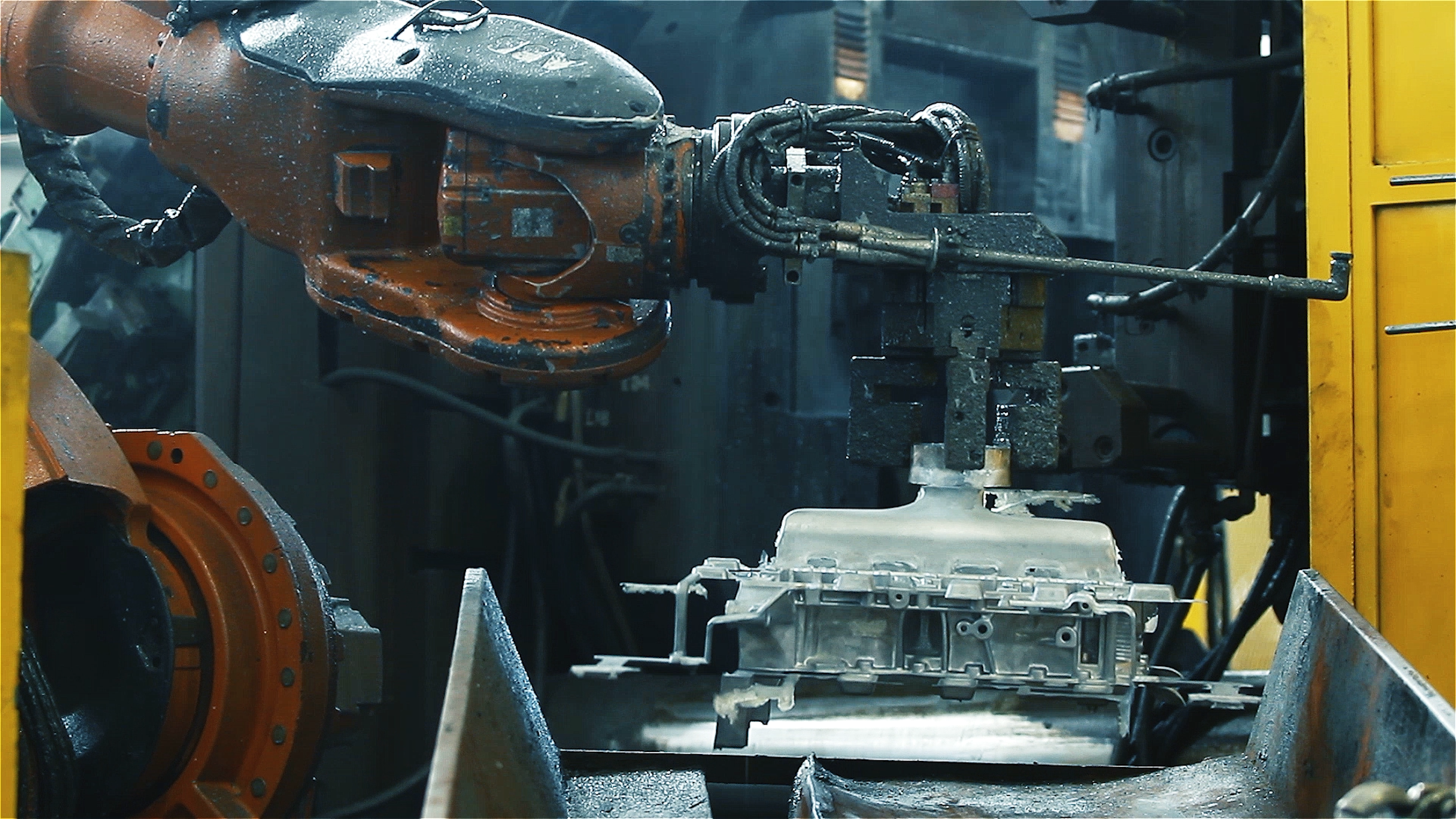 Orange industrial robot arm handling a metal casting