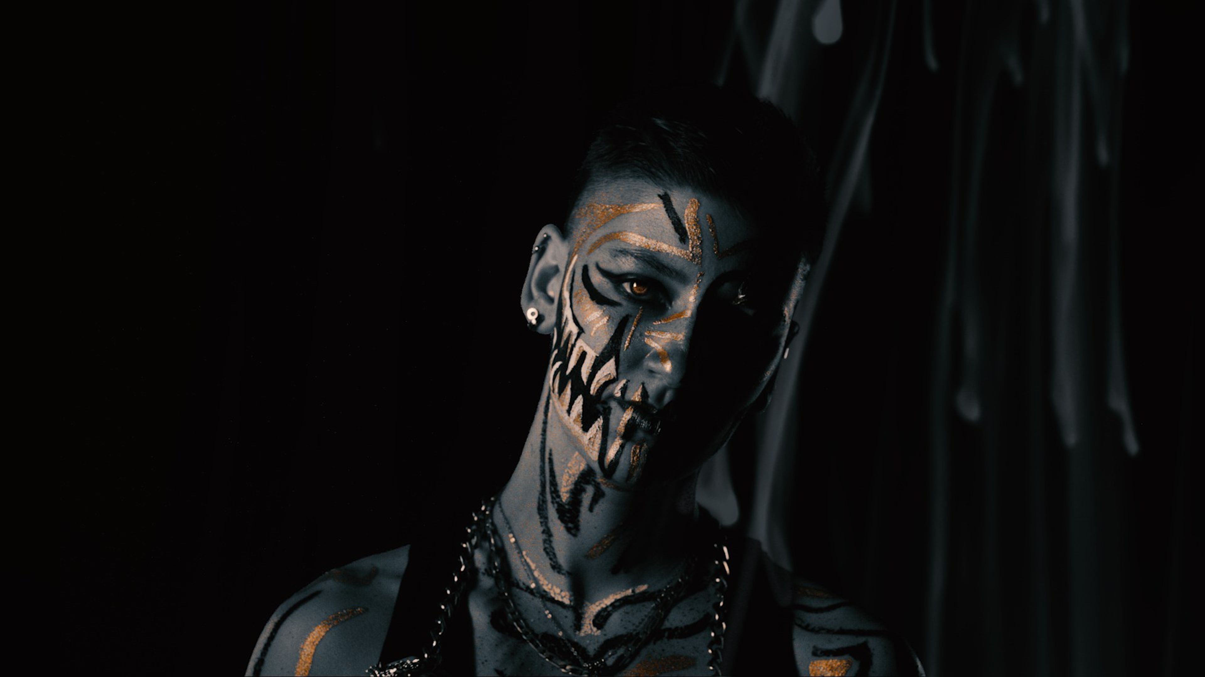 Dark portrait with black fang markings and gold shimmer on the face, one half lit
