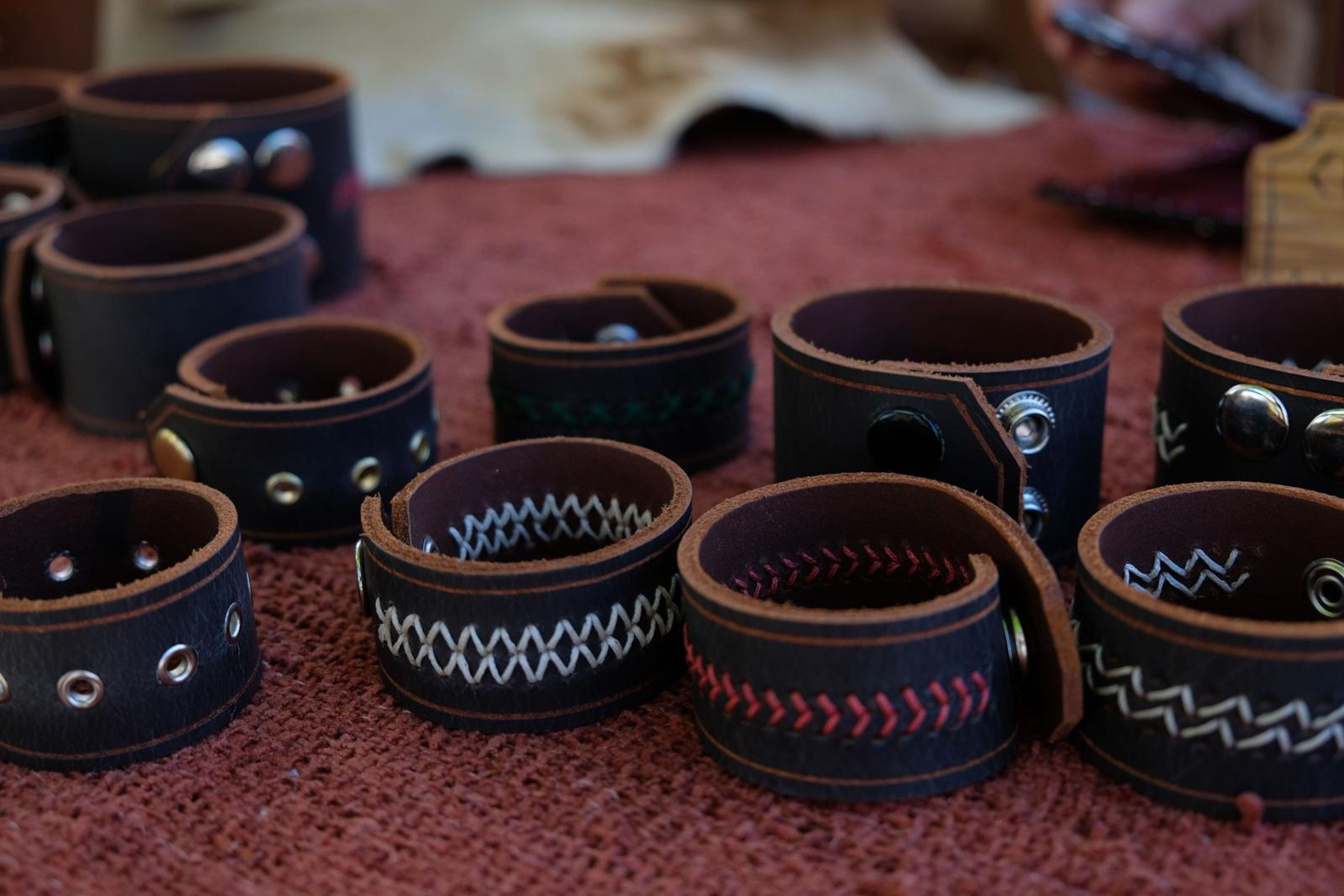 Row of dark leather cuffs with white, red and green hand-stitched patterns