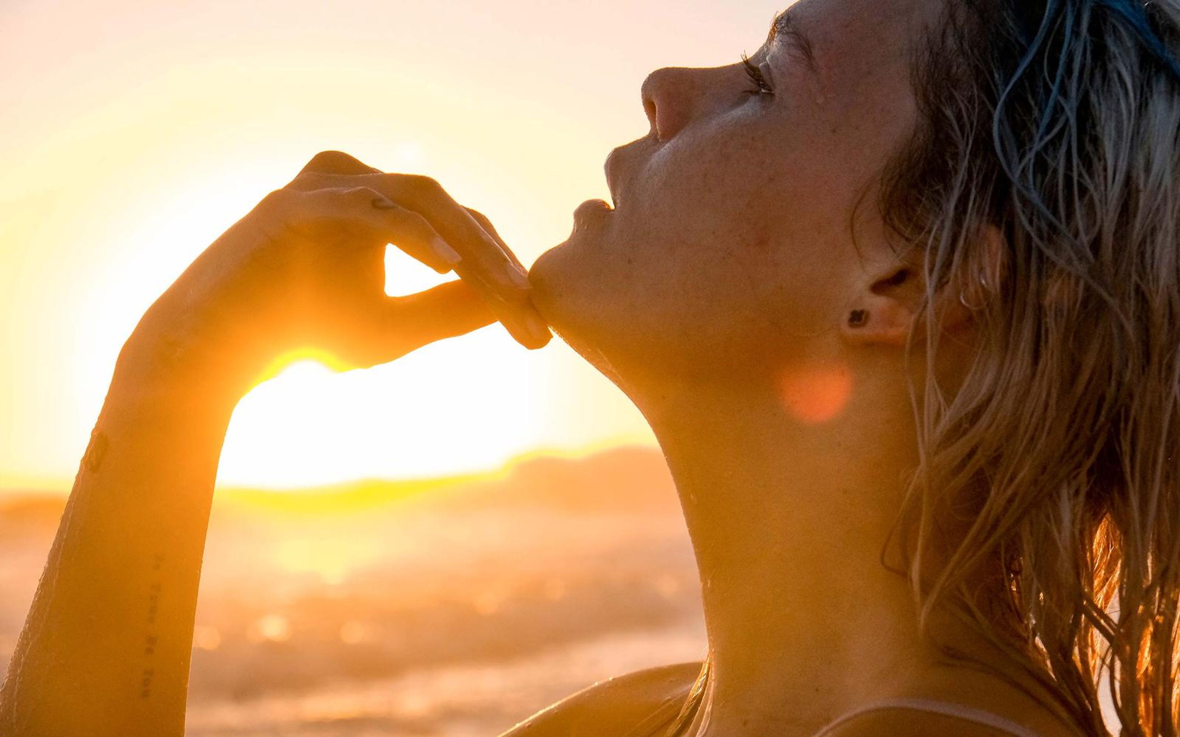 Profile portrait with eyes closed and chin lifted, fingers resting beneath her jaw, sunset haze behind