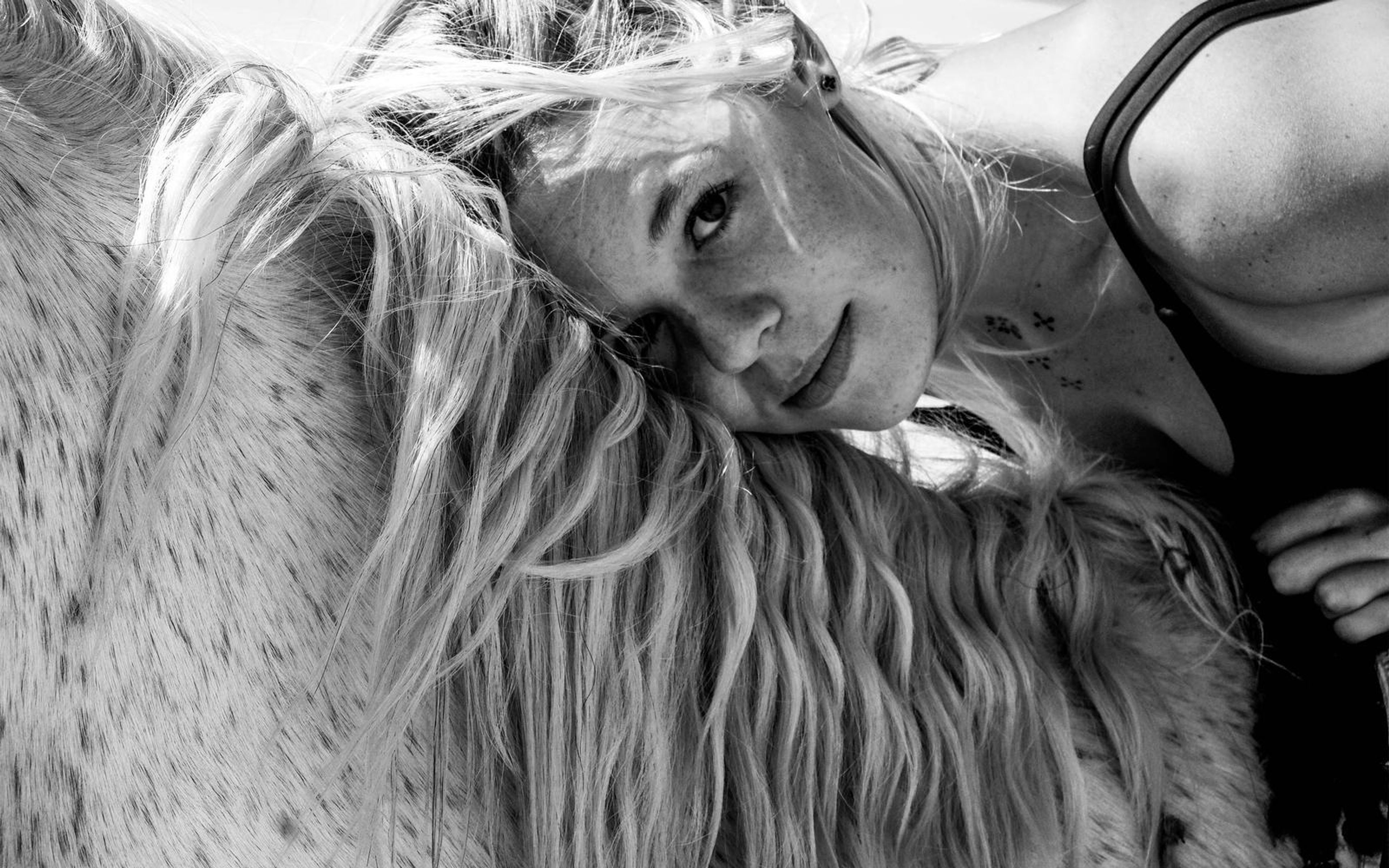 Black and white portrait of a woman looking up over a horse's mane with a soft smile