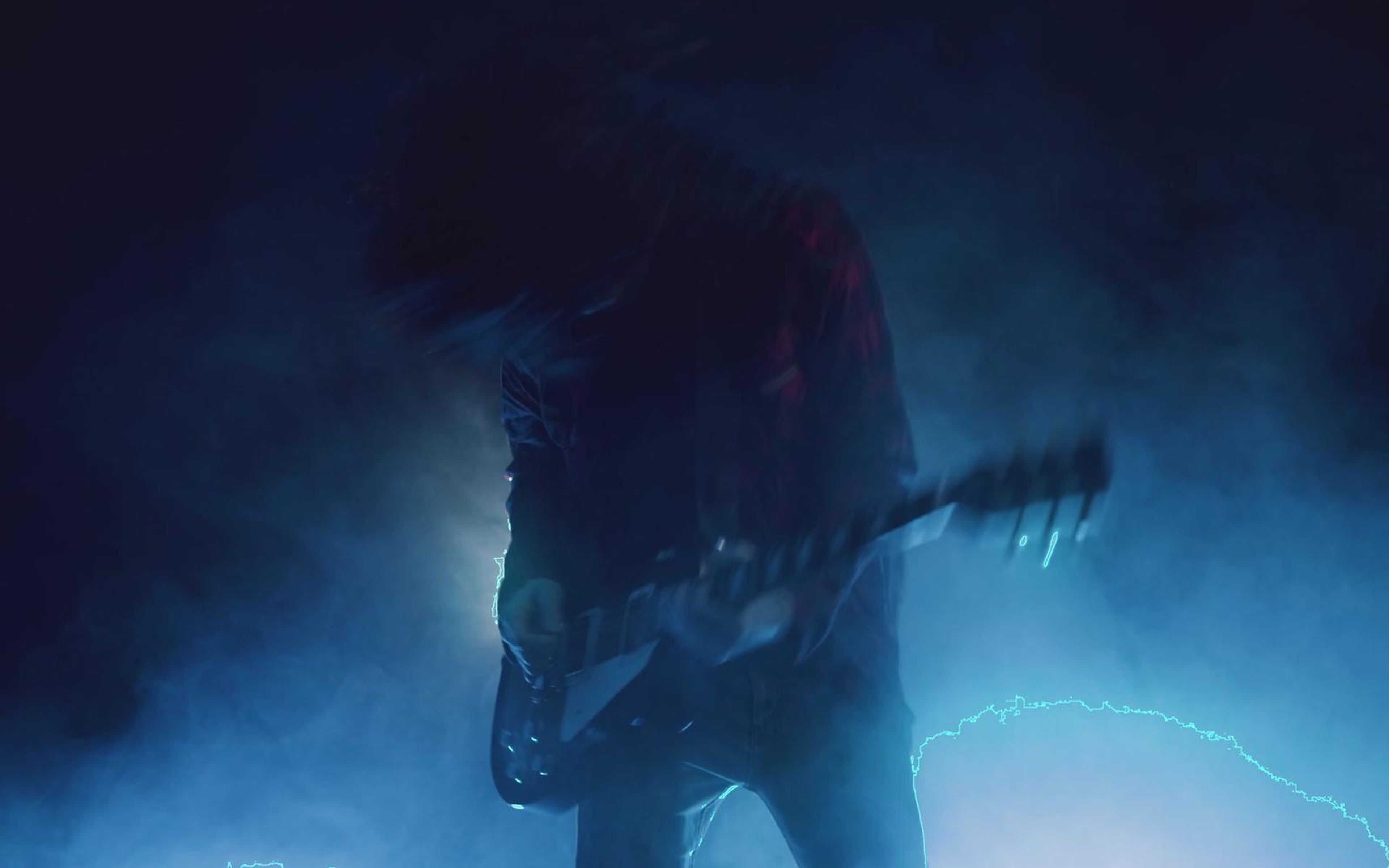 Long-haired guitarist in a plaid shirt playing in blue stage smoke
