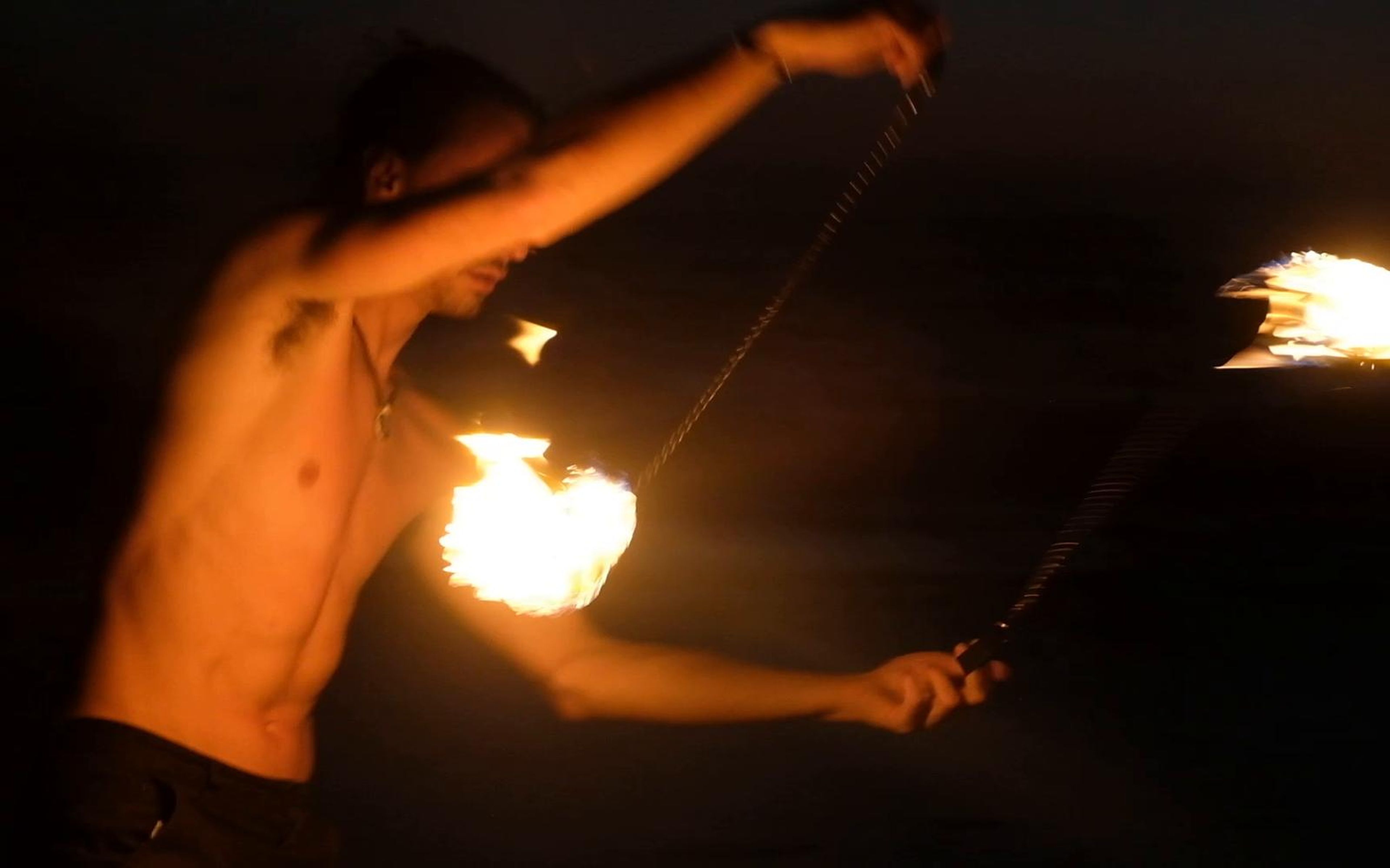 Shirtless performer swinging fire poi with the flames blurring in motion