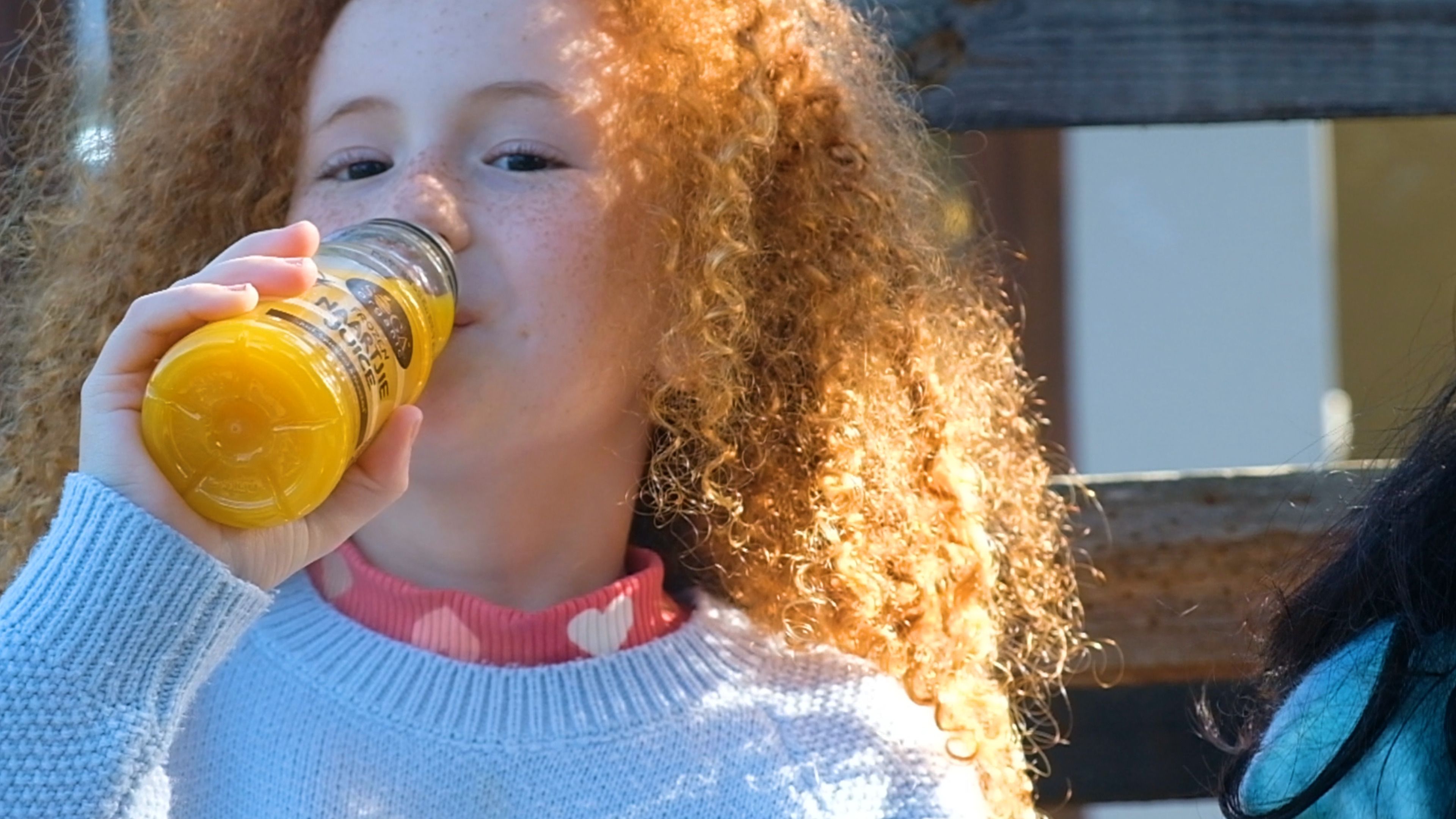 Girl drinking SOGA orange juice from a small bottle outdoors