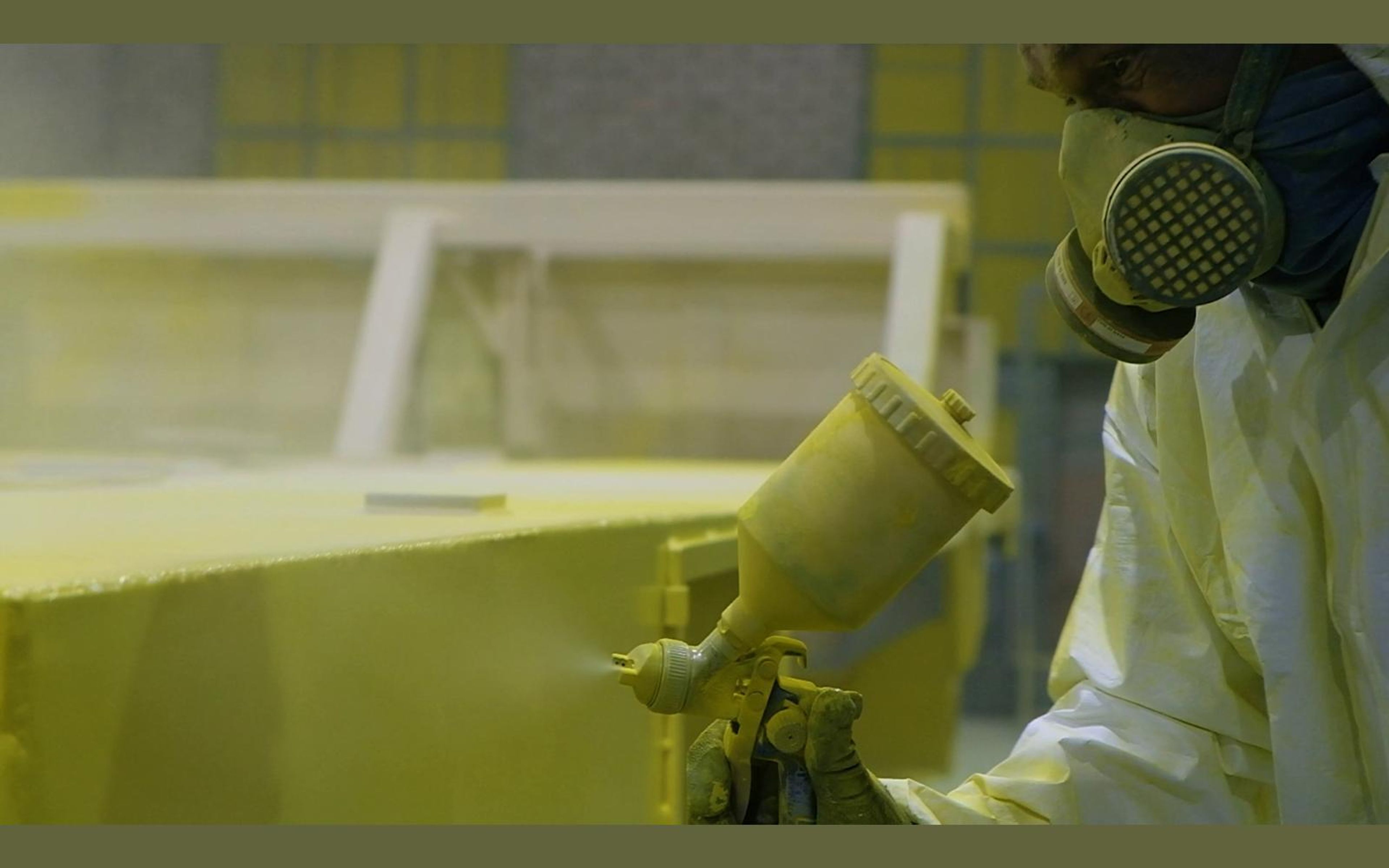 Spray gun with a cup of yellow paint held against a steel panel
