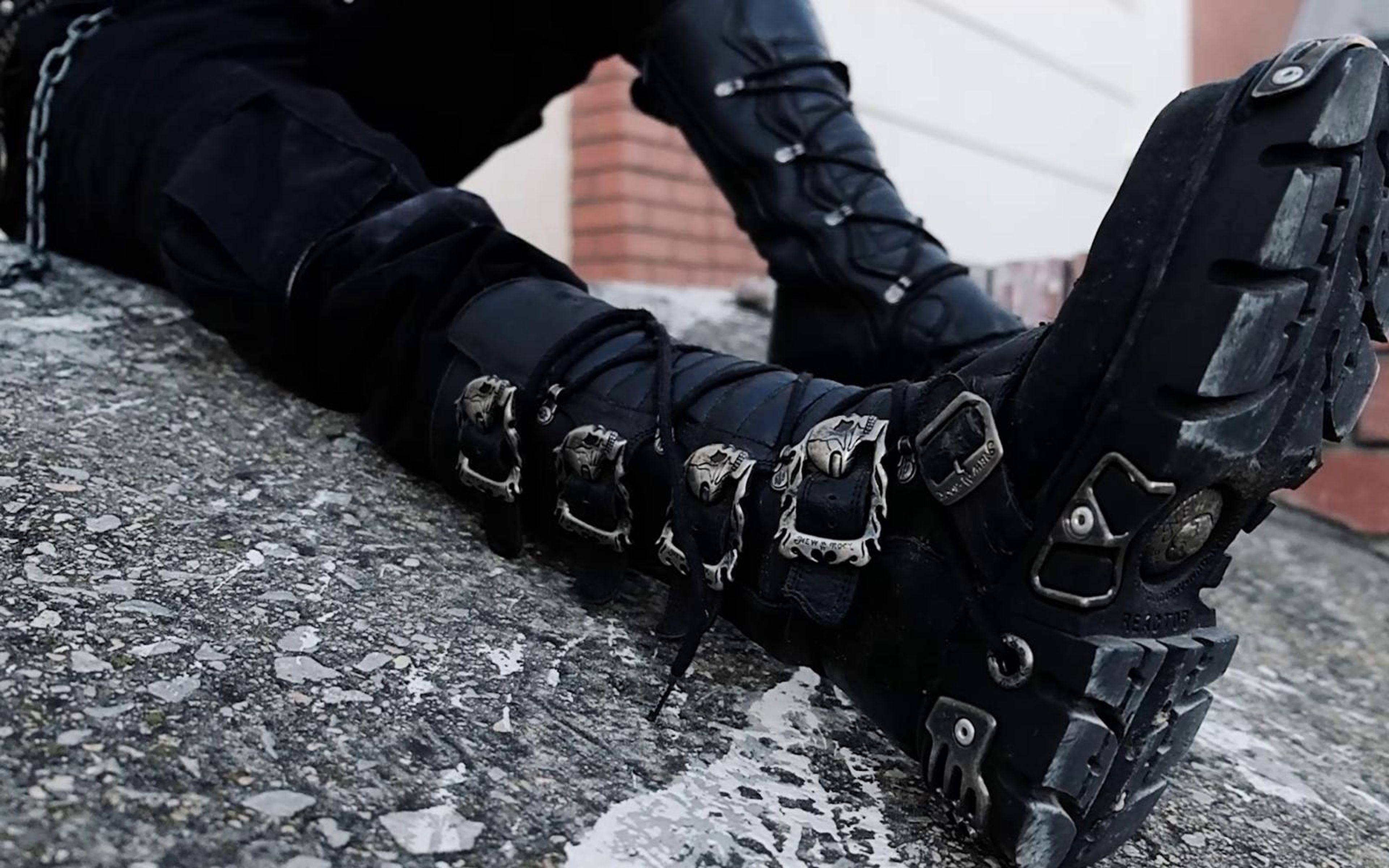 New Rock boots with skull buckles and chunky soles propped on a rough concrete slab with red brick behind