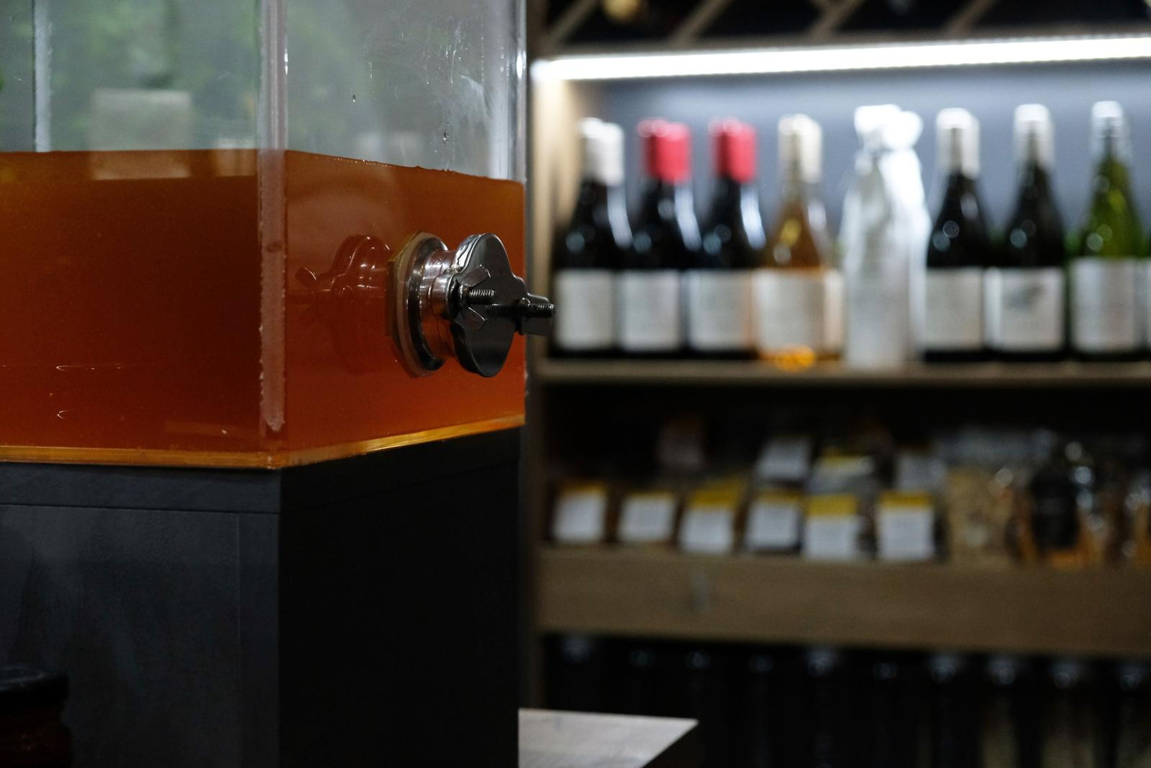 Glass drinks dispenser beside a wall of wine bottles
