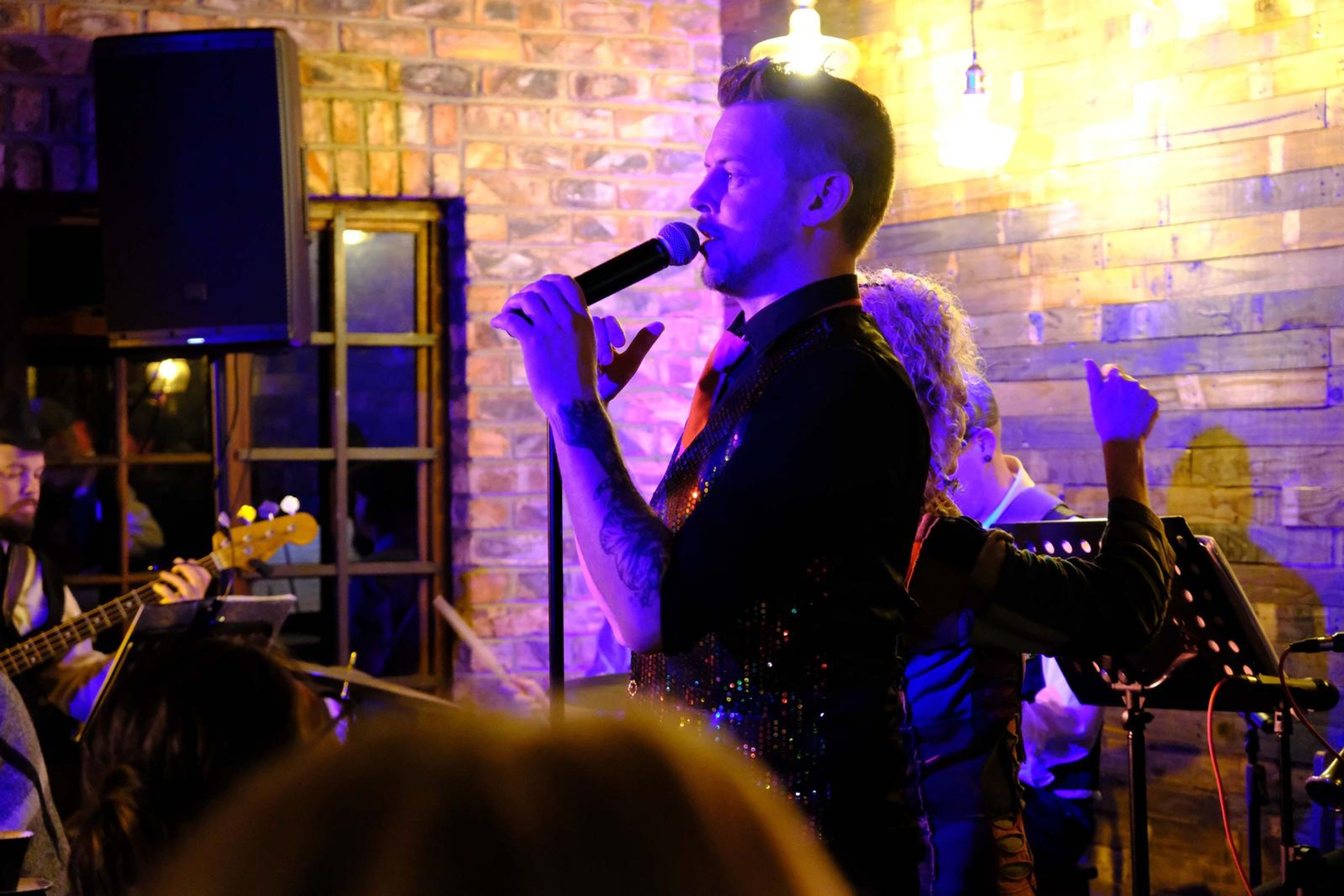 Lead singer in a sequin vest singing to the room