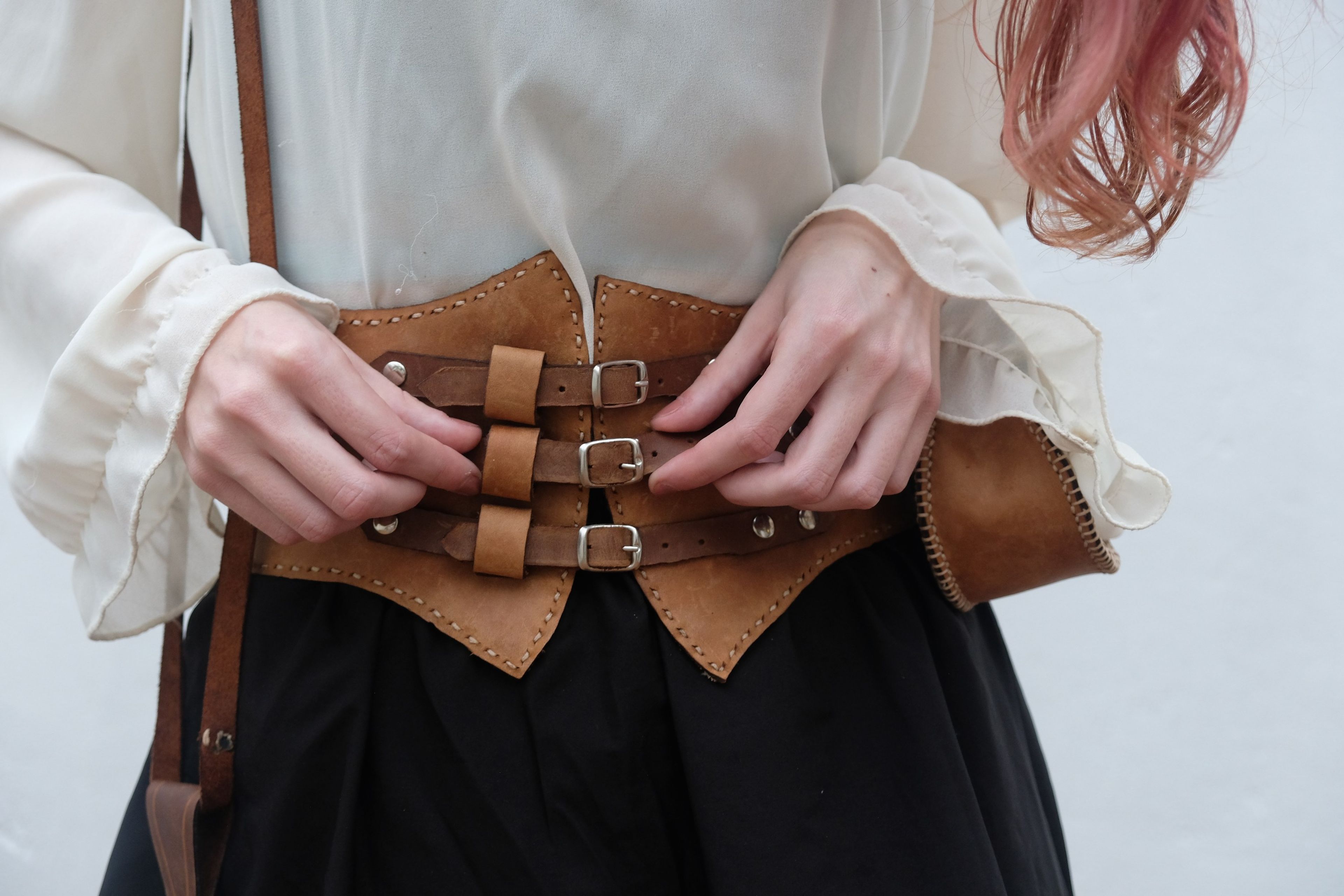 Hands adjusting the straps of a leather corset belt over a black skirt