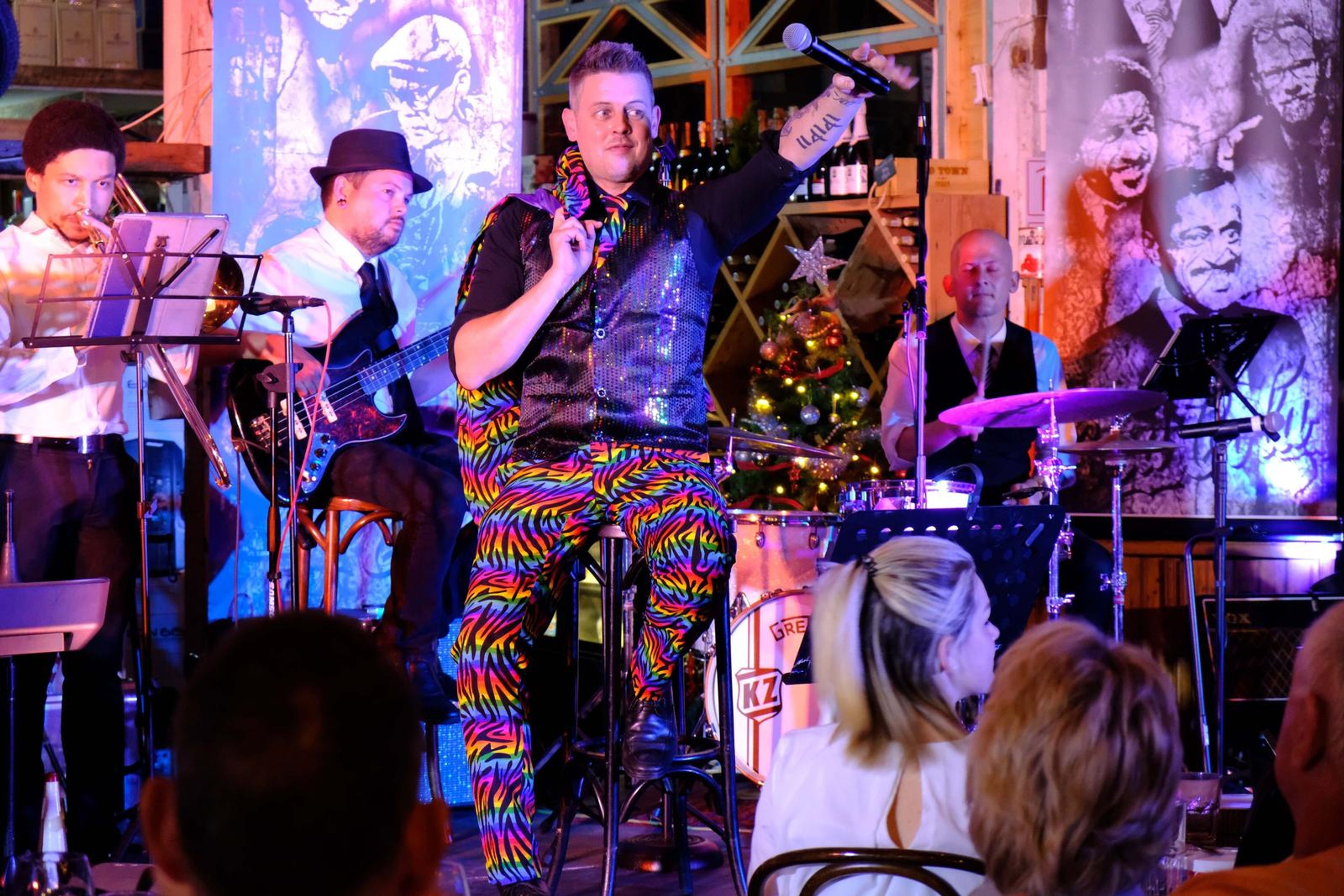 Singer in rainbow trousers celebrating in front of a Christmas tree