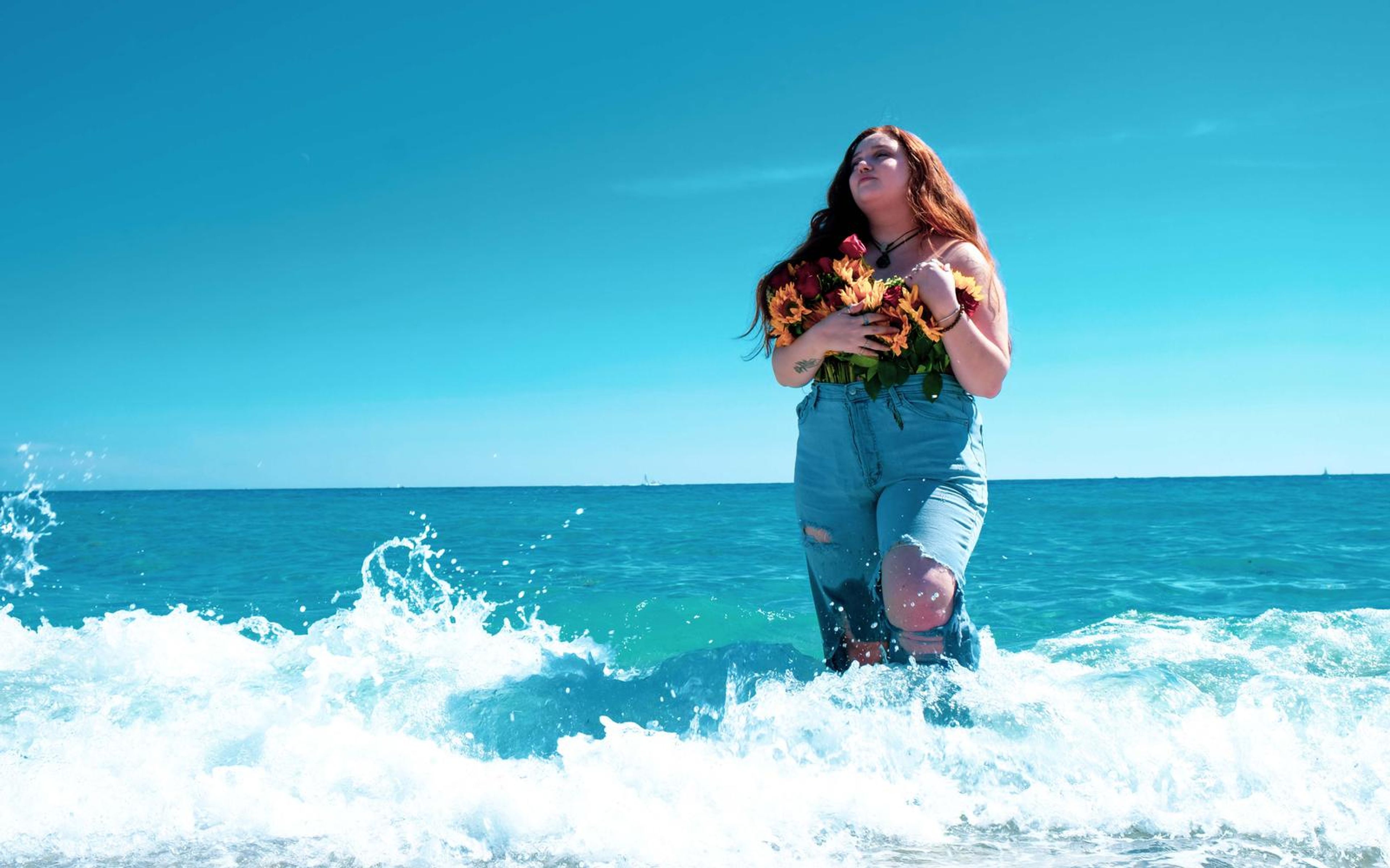 Model with face lifted standing in saturated teal water, white wave foam around her knees
