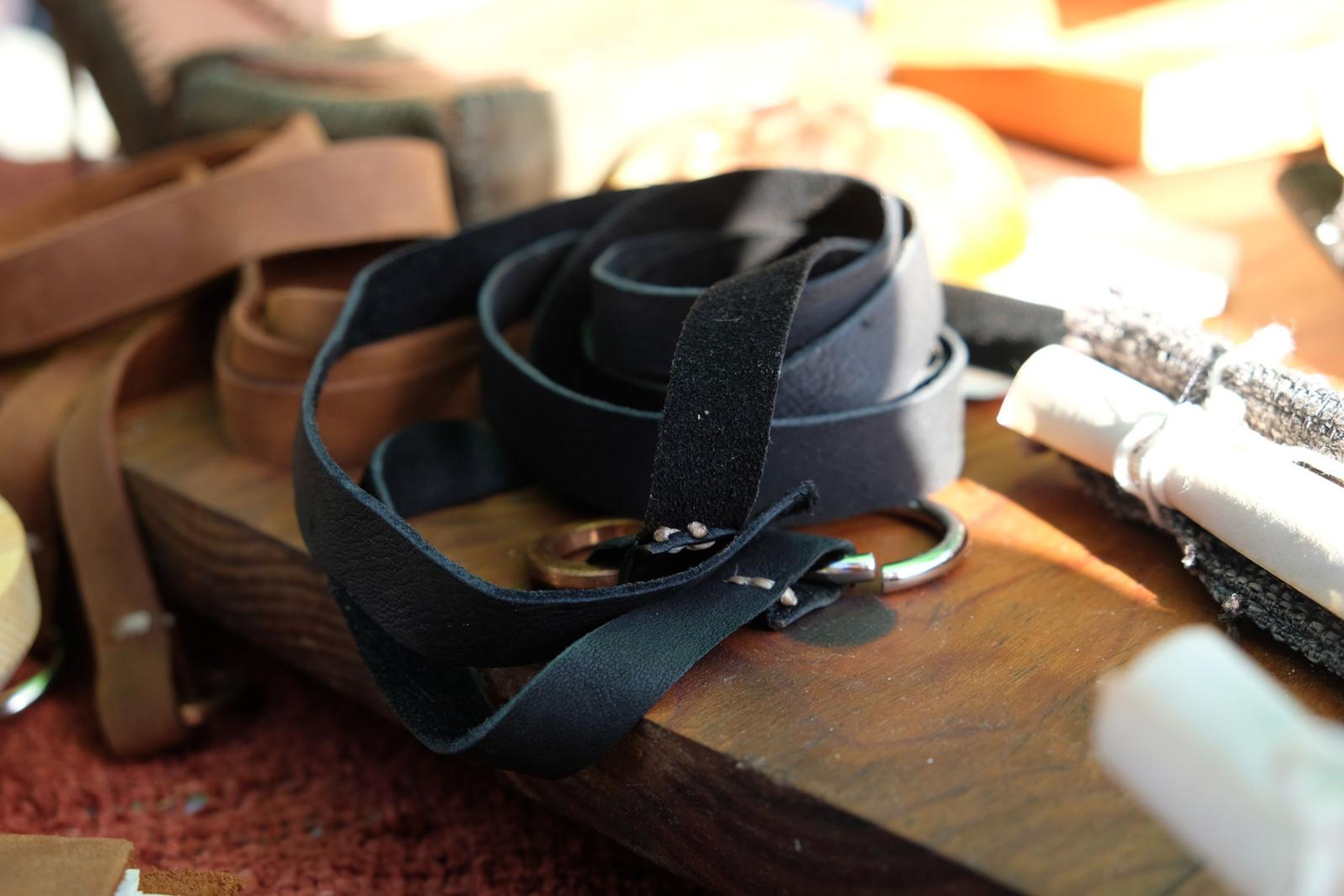 Close-up of a black leather strap with a metal ring buckle on a wooden board