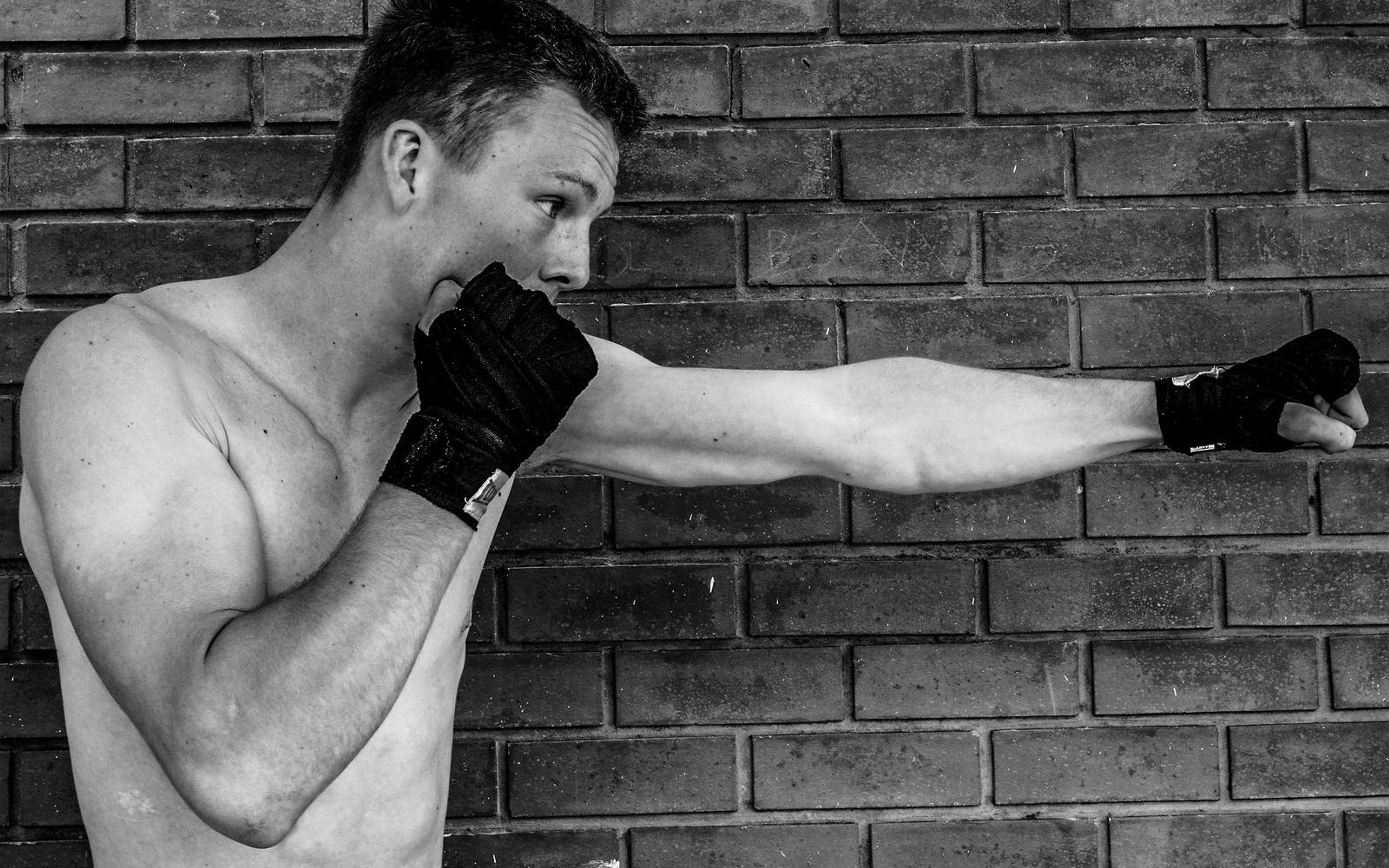 Black and white portrait of a man mid-punch with his guard hand at his face, brick wall behind
