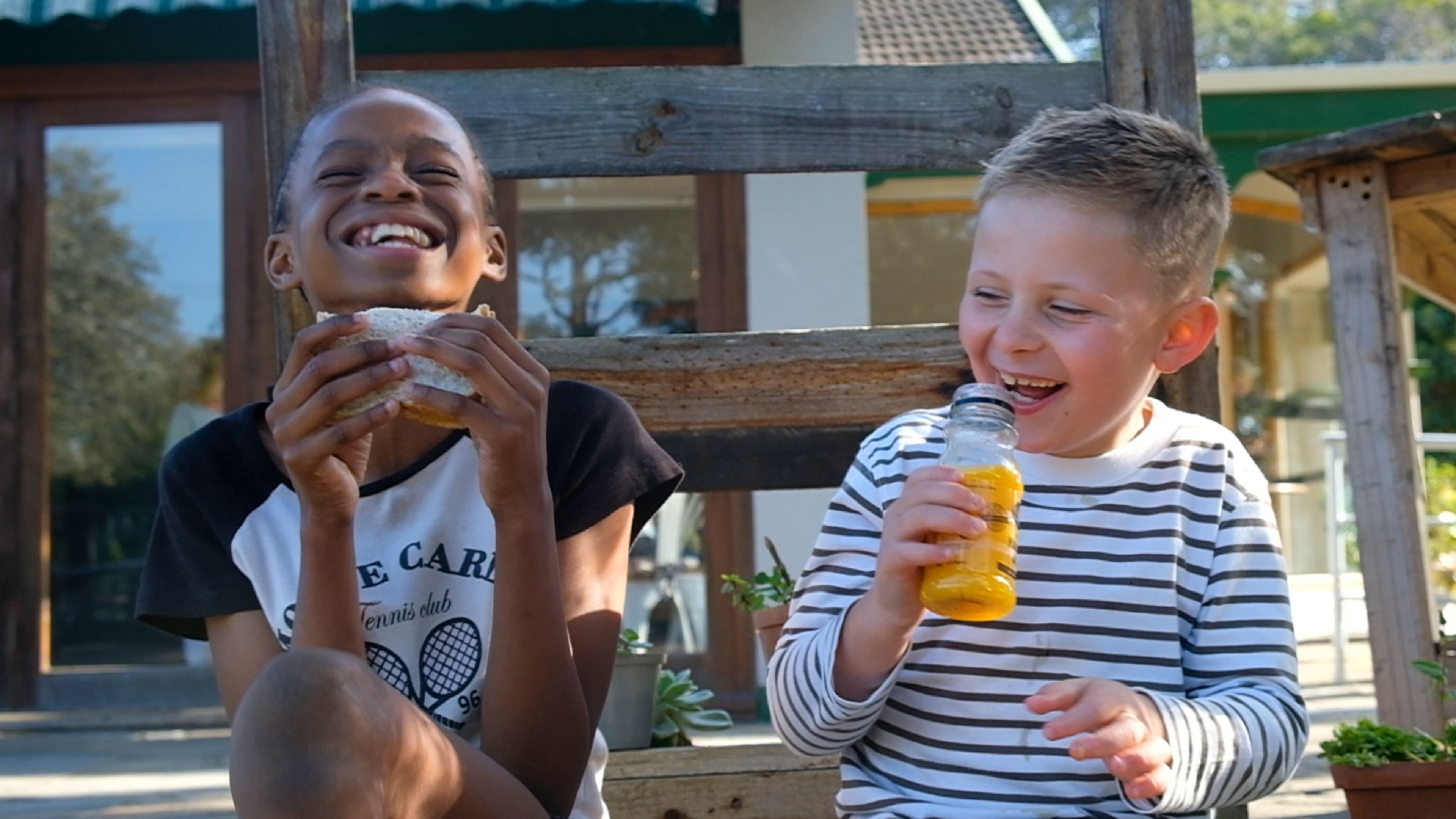 Two children laughing together, one holding a bottle of juice