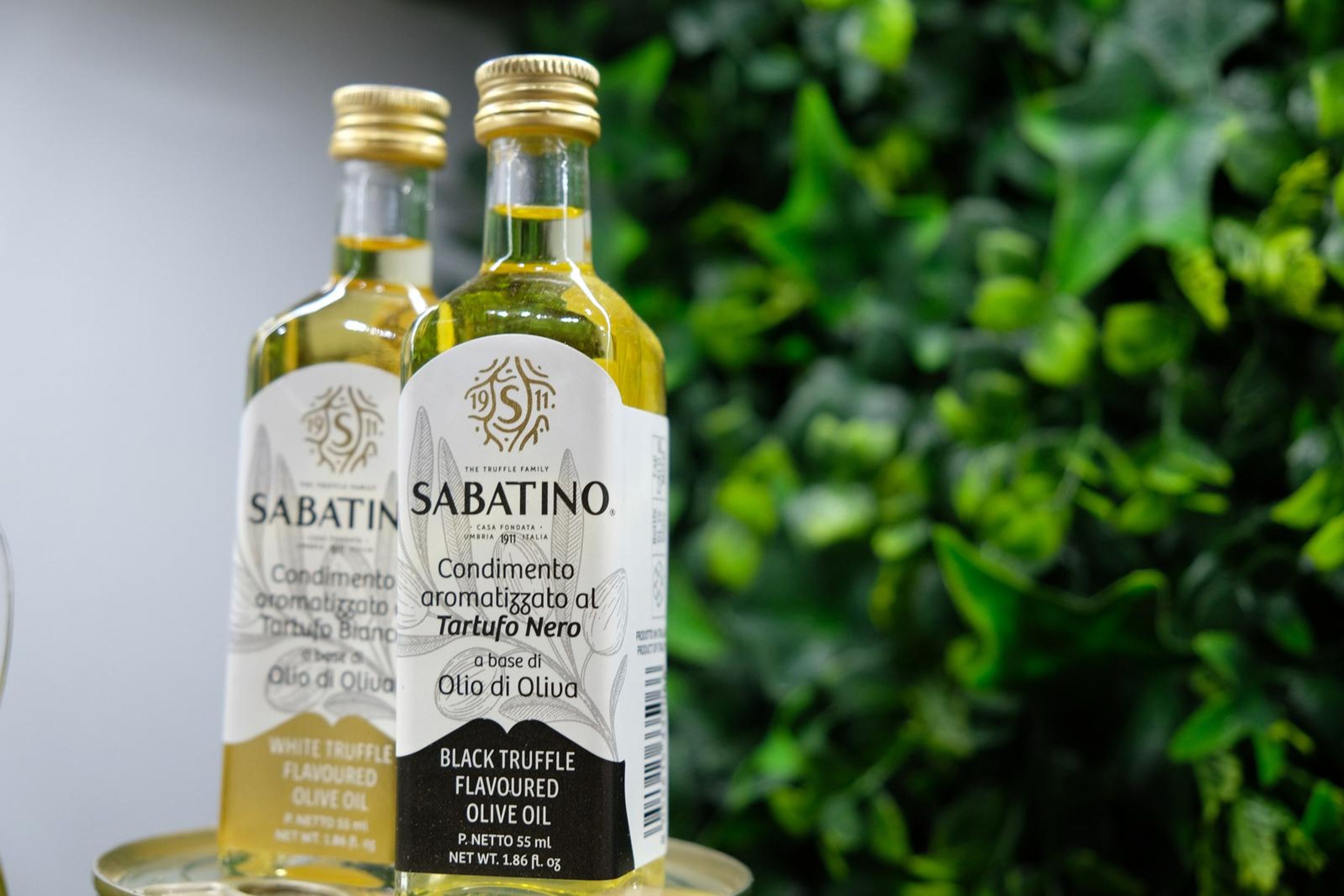 Two bottles of truffle olive oil in front of a green wall